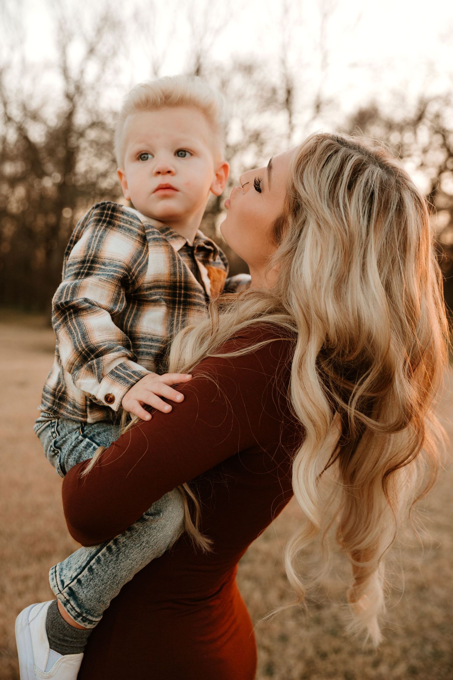 Parent and child share tender moments in a field at sunset wearing coordinating plaid and brown outfits.