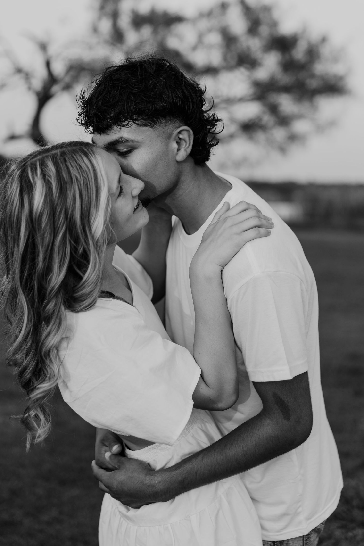 Black and white photos of romantic couple in white shirts embracing and sharing intimate moments outdoors.