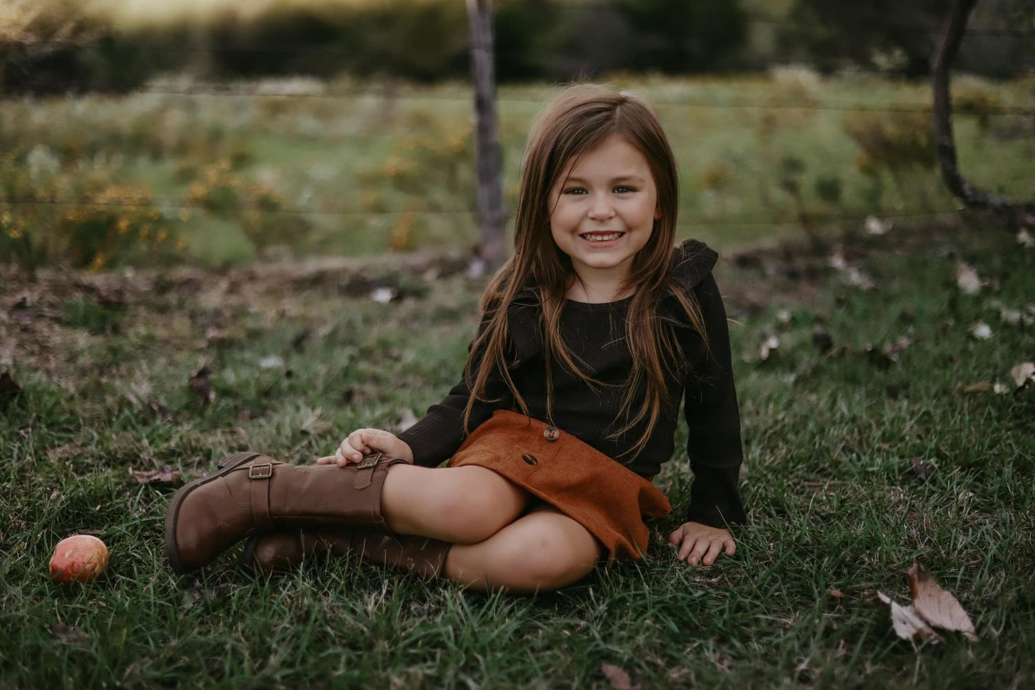 Child sitting on grass with autumn leaves and natural outdoor lighting.