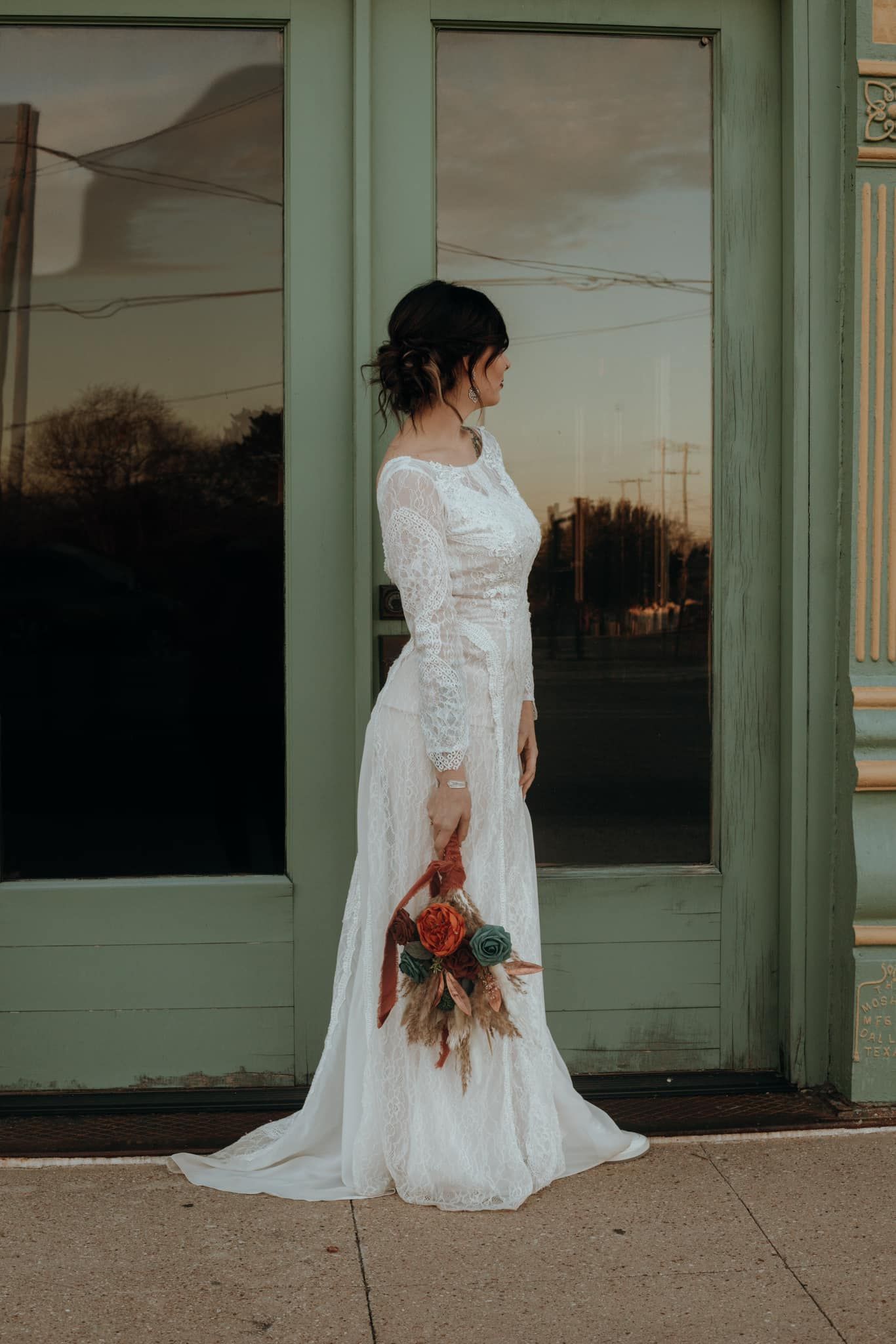 Bride in elegant lace wedding dress poses by vintage green doorway.