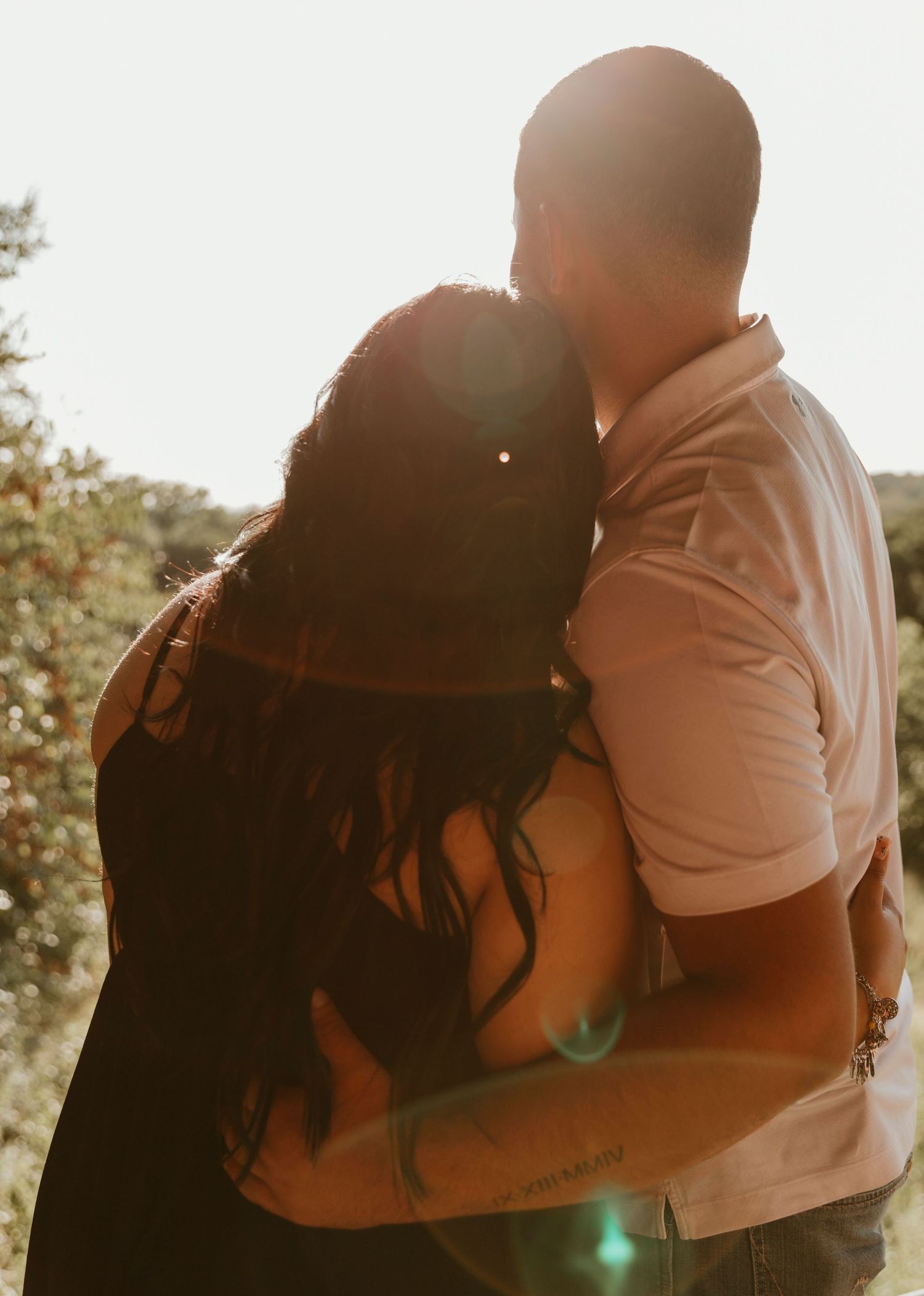 A romantic silhouette of a couple embracing in warm sunlight with lens flares and trees in the background.