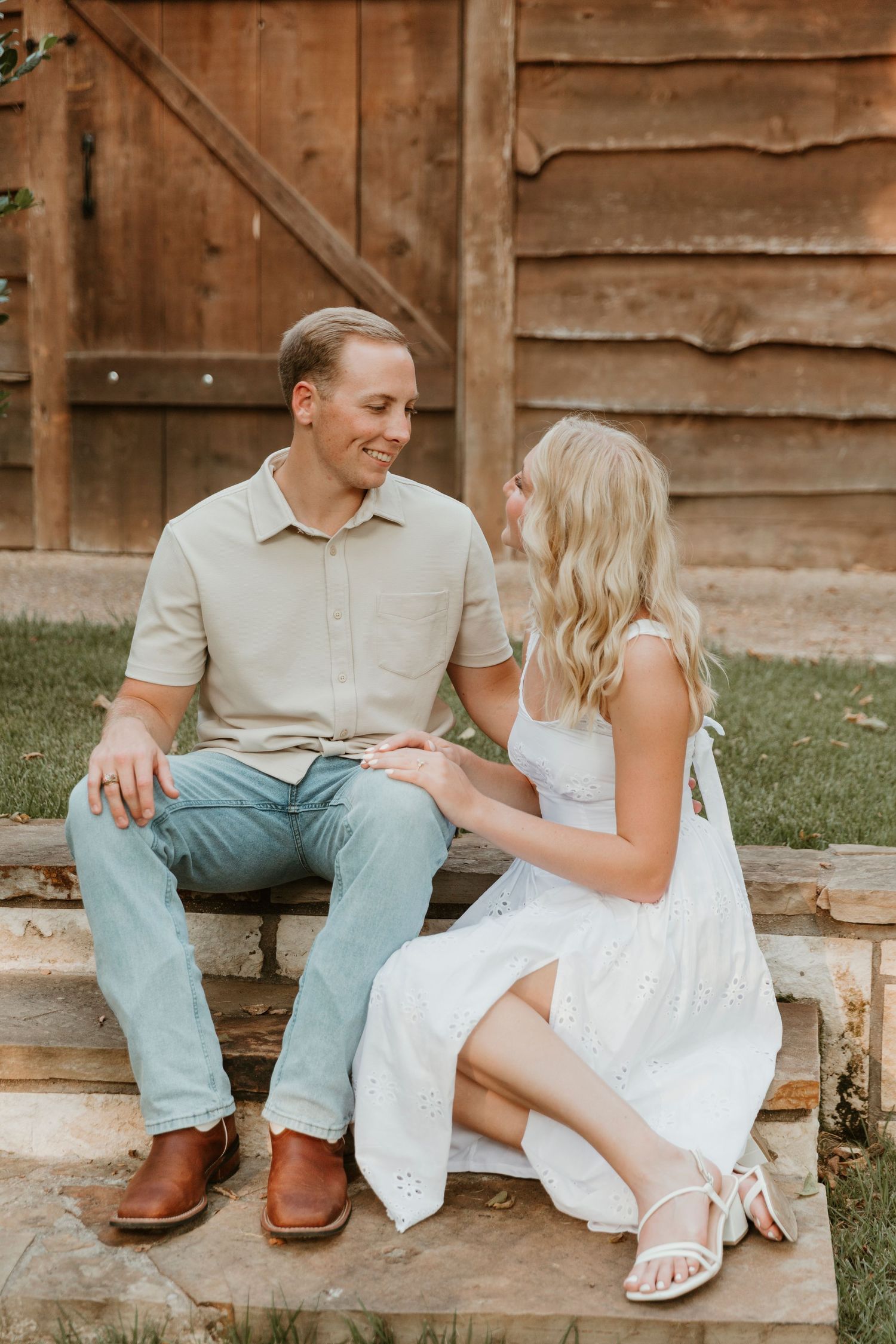Couple sits together on rustic wooden steps in matching light outfits sharing sweet candid moments.
