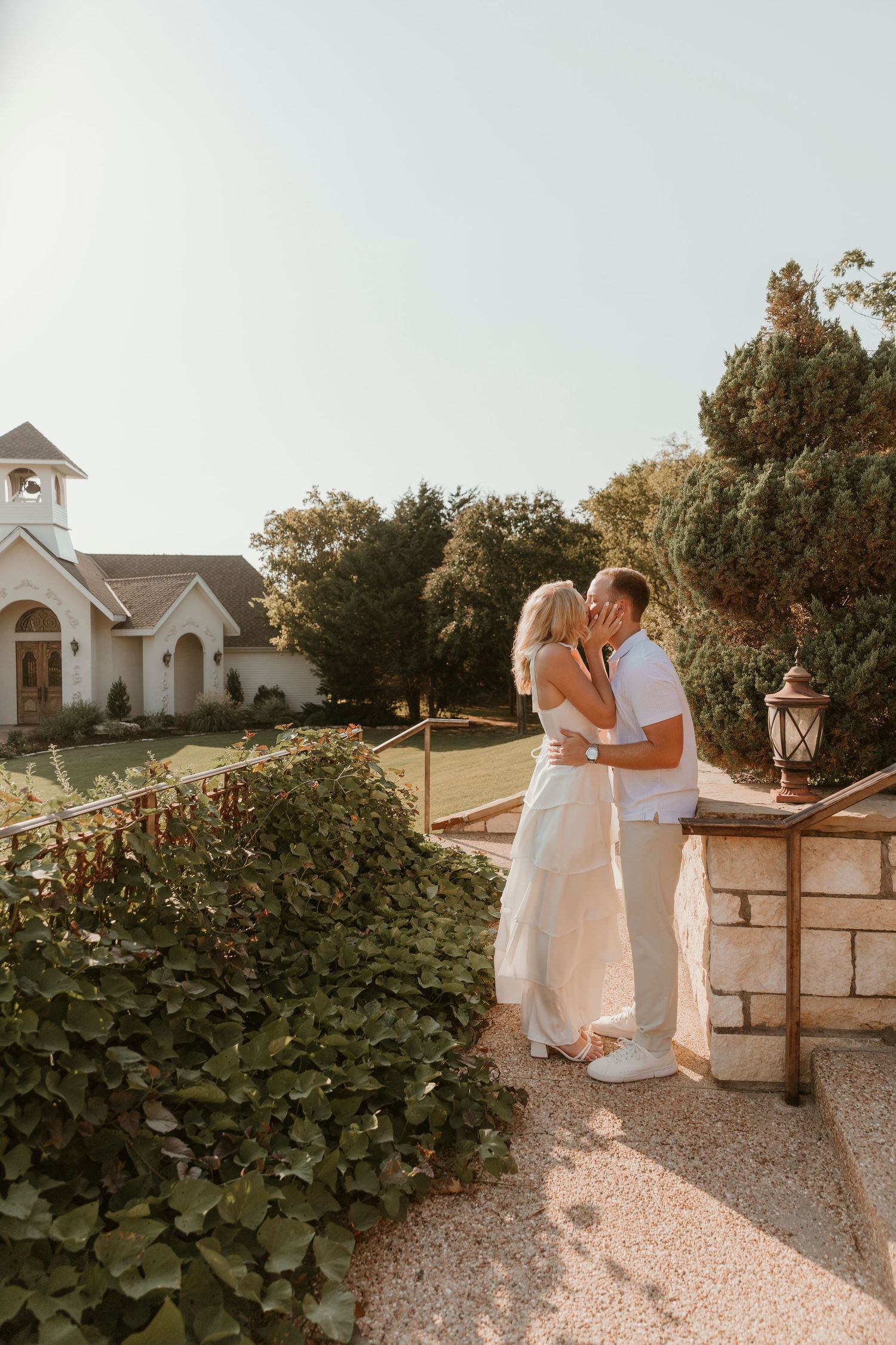 A couple shares an intimate moment on a stone patio with a beautiful church backdrop at golden hour.