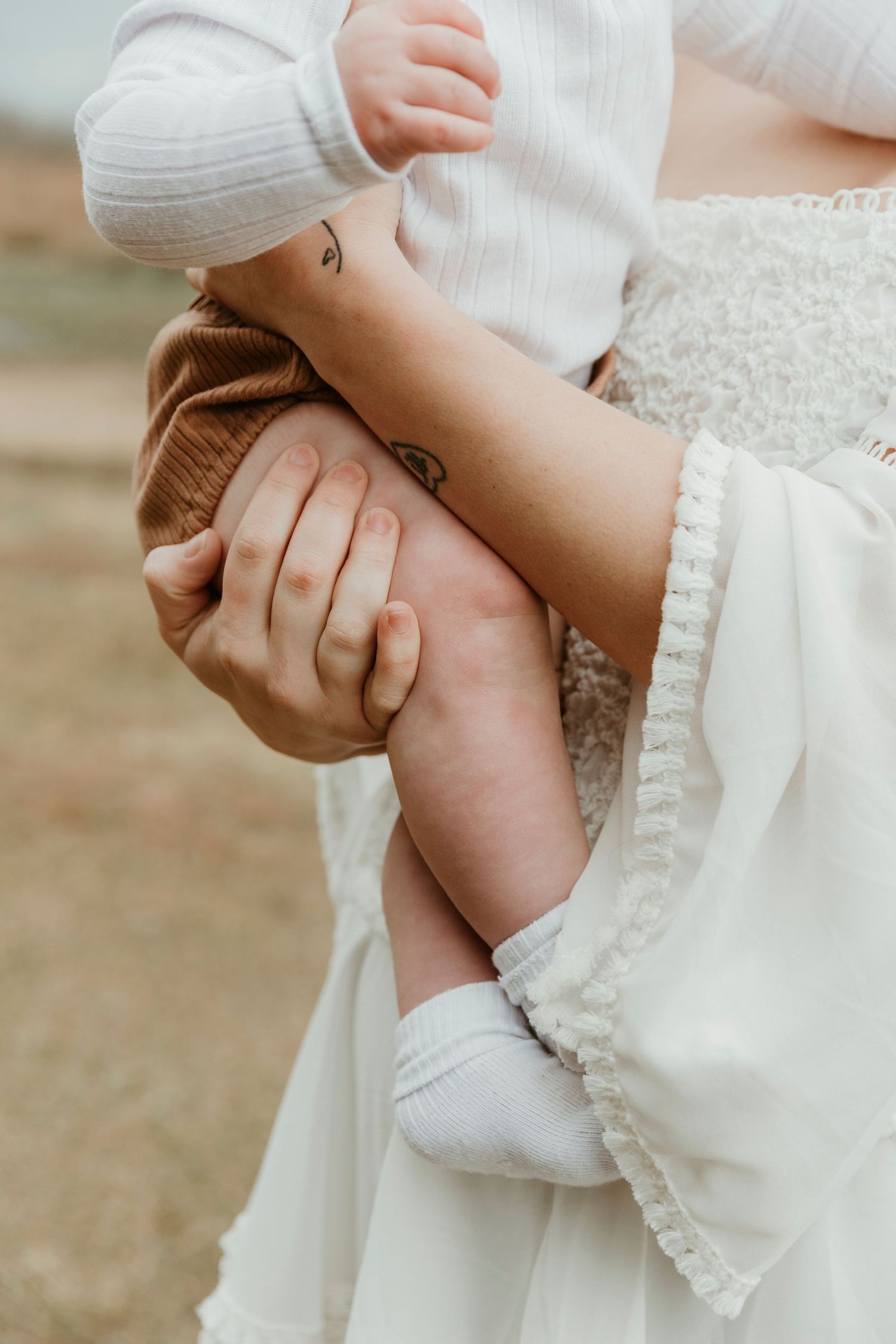 Close-up of gentle hands holding baby's leg in white clothing.