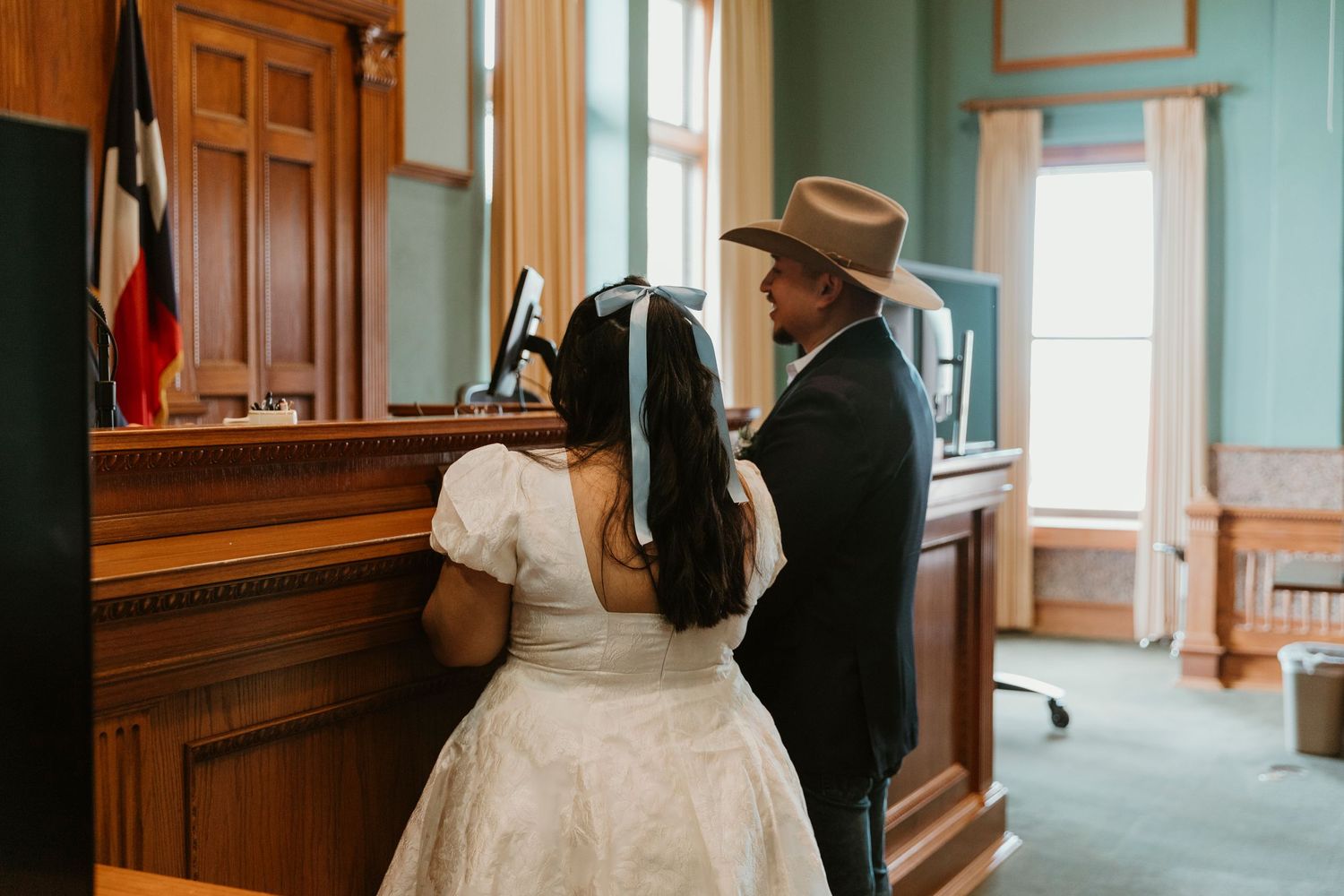 Wedding ceremony in a historic courthouse with wooden paneling and Texas flag visible.