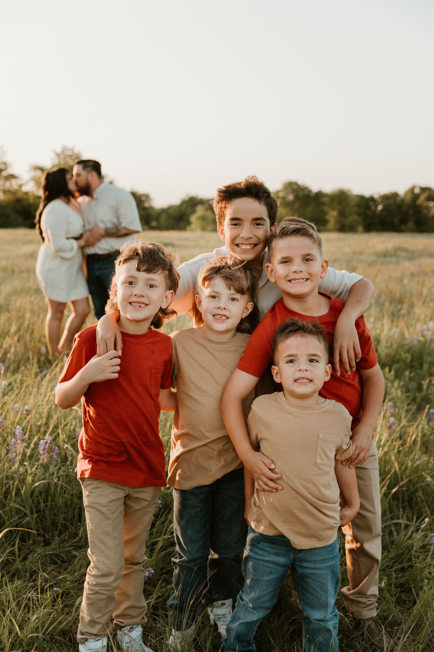 Group of children posing together in casual attire in a golden field at sunset.