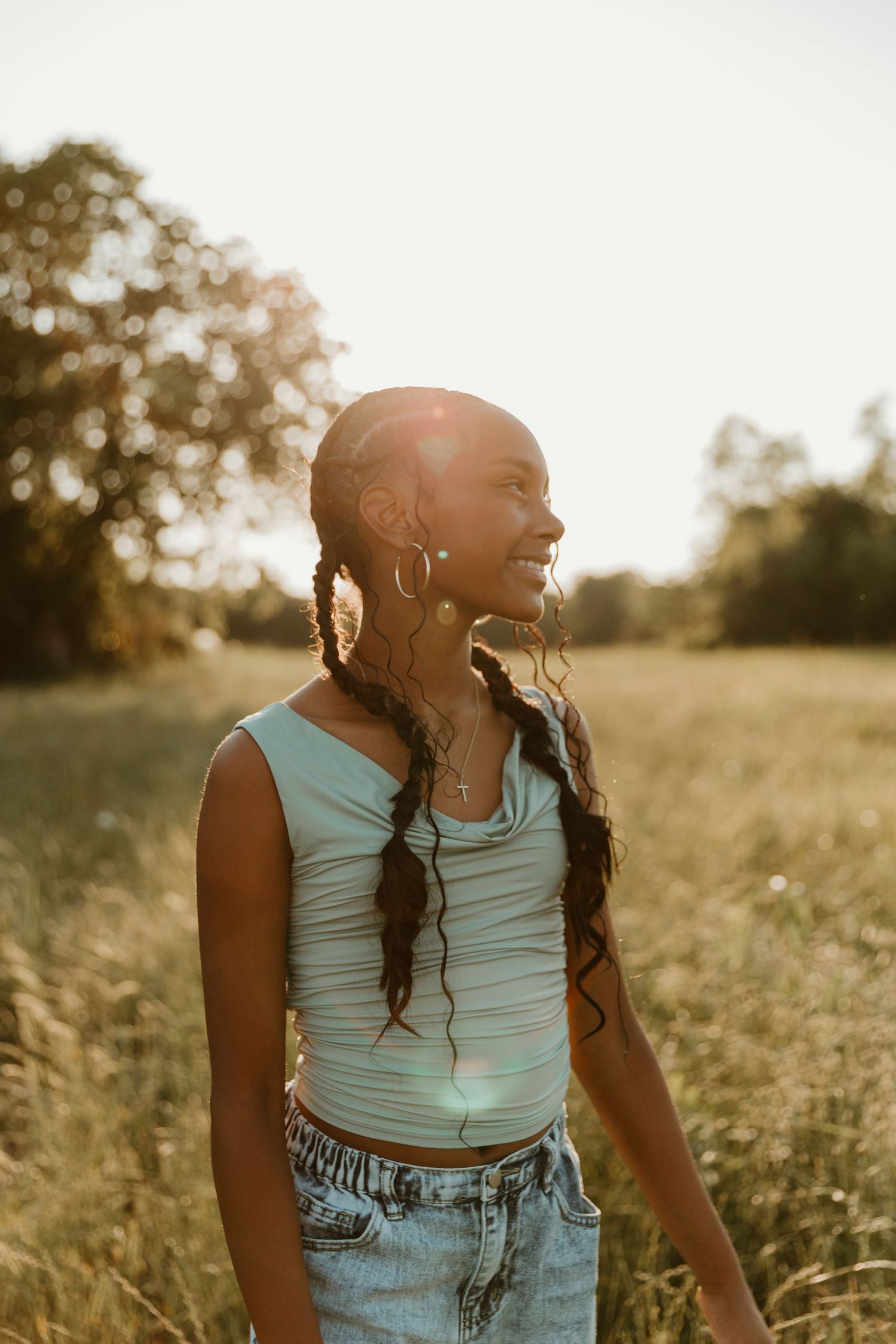Person in turquoise tank top and jeans laughing joyfully in golden evening light.