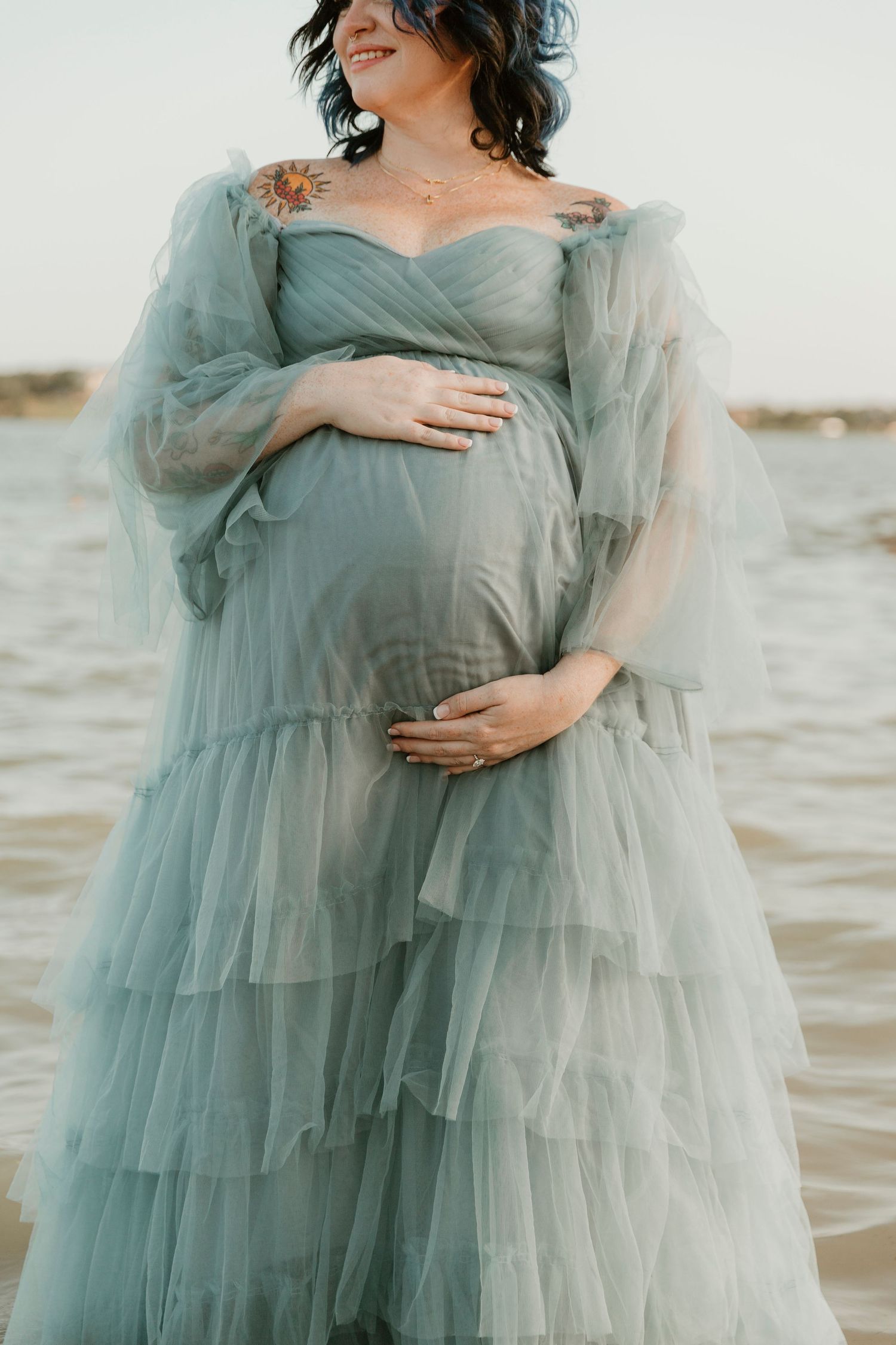 A peaceful maternity moment captured in a dreamy seafoam green gown by the water.