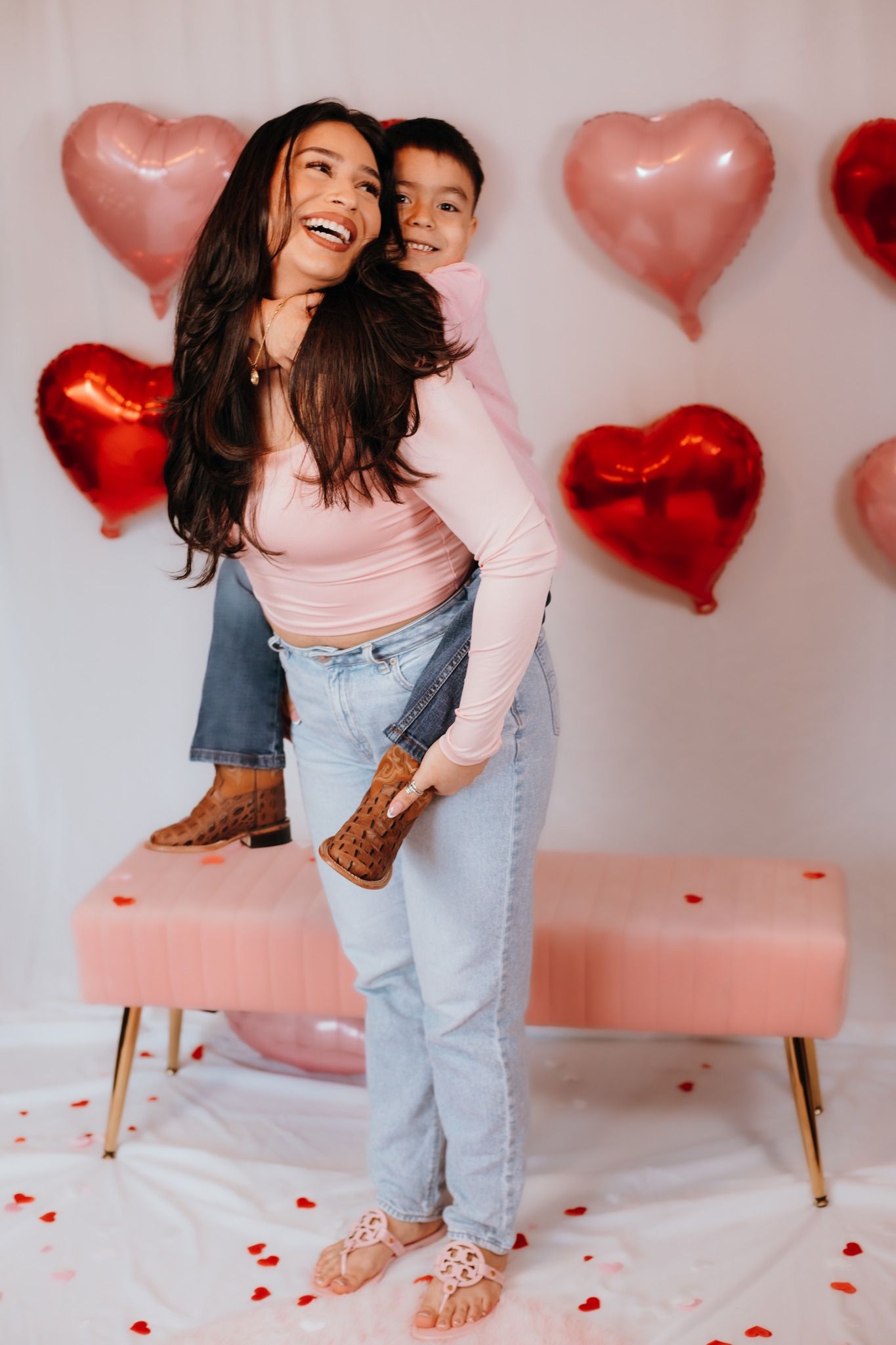 Joyful piggyback ride moment against a backdrop of floating pink and red heart balloons.
