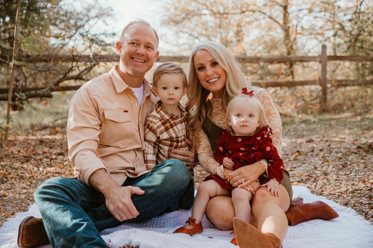 A family wearing coordinated fall outfits sits together on a blanket during an autumn outdoor photo session.