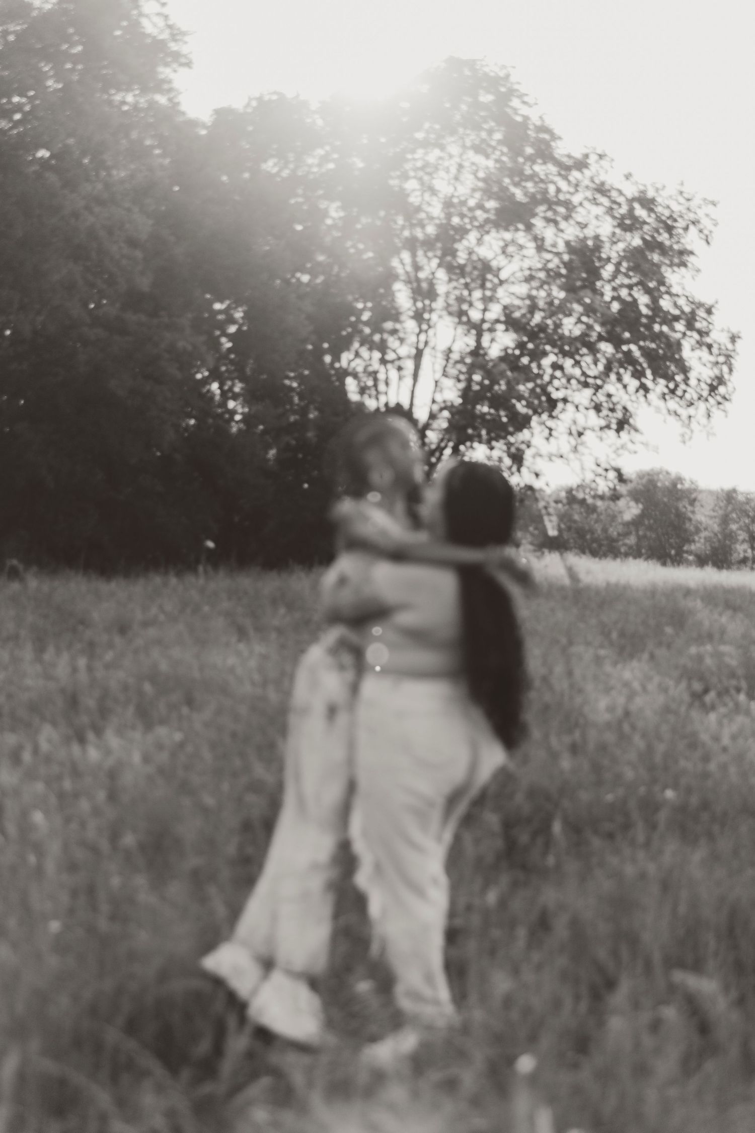 A black and white photo captures two people embracing in a misty field.