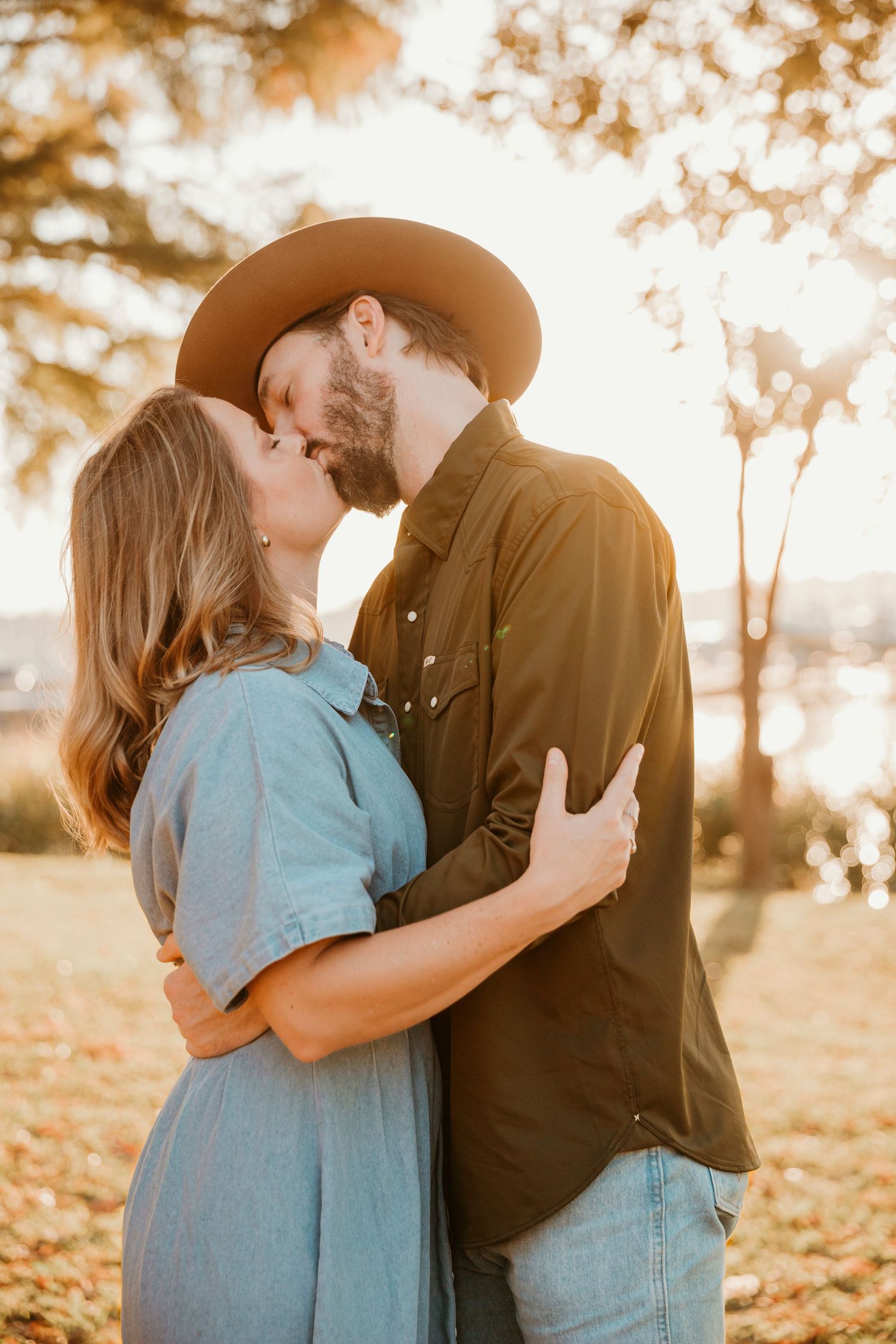 A couple embraces in a romantic moment outdoors during golden hour with autumn trees in the background.