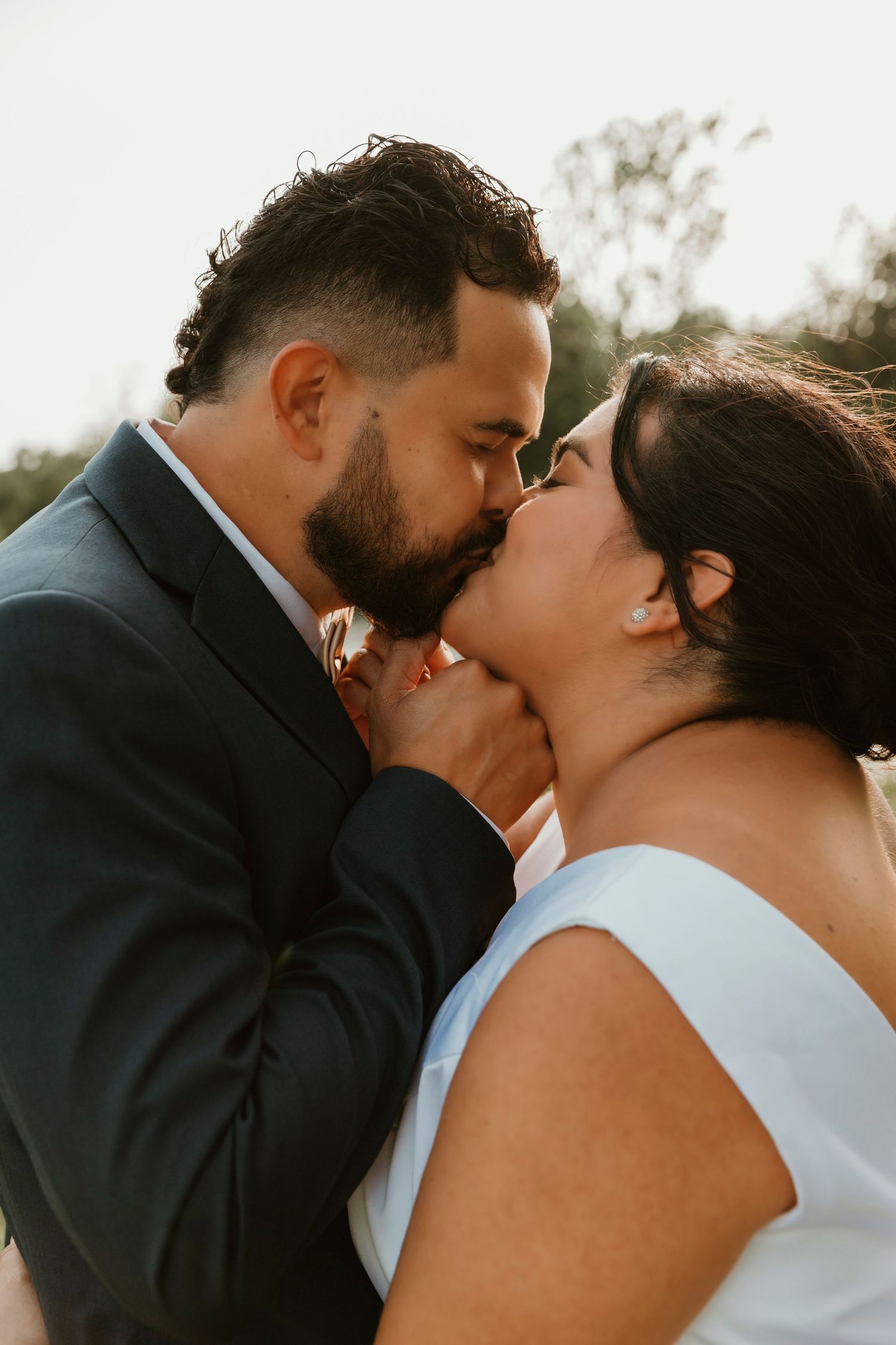Romantic wedding couple sharing intimate kisses against a sunset backdrop.
