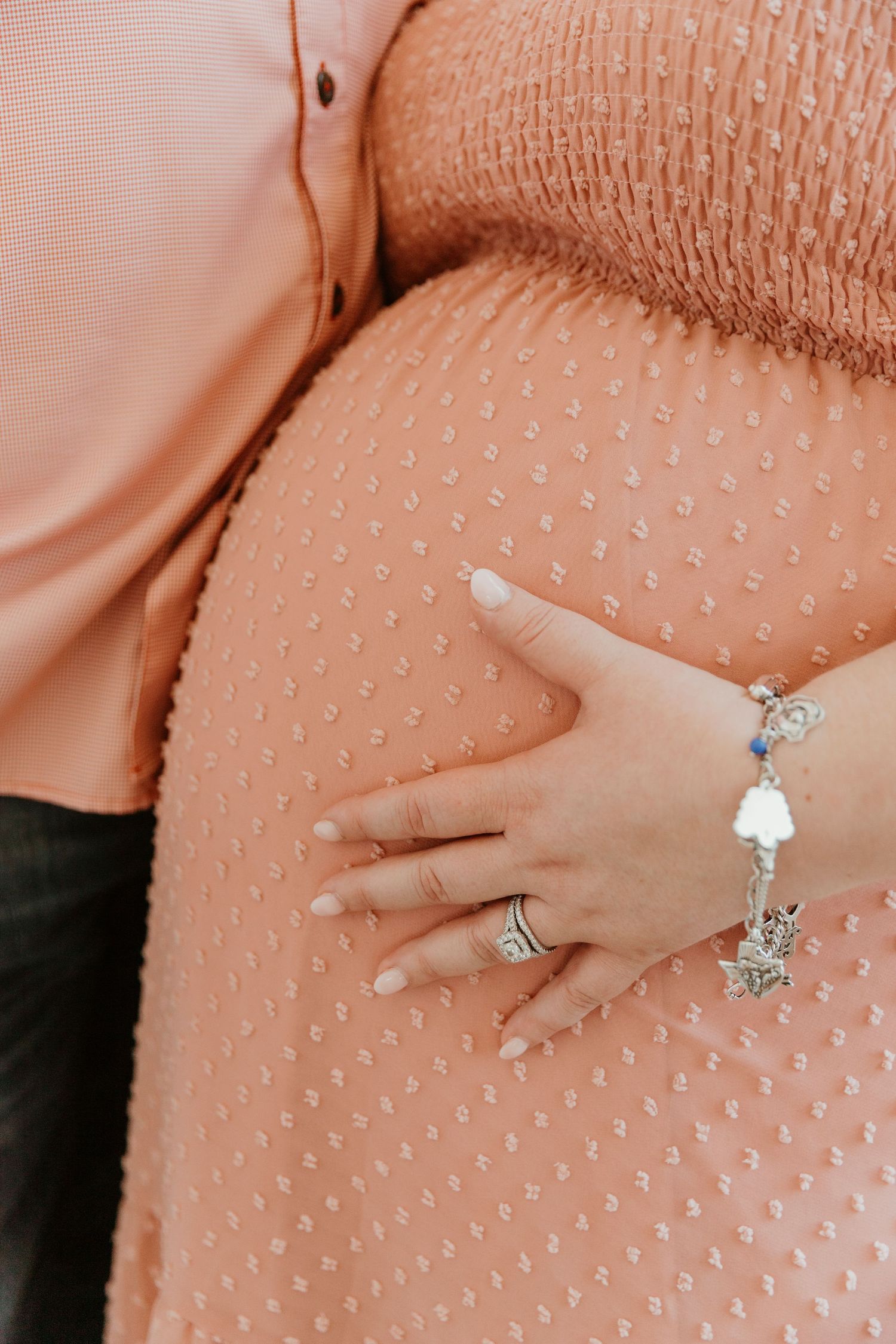 Multiple engagement rings are displayed on a hand against a pink dotted fabric background.