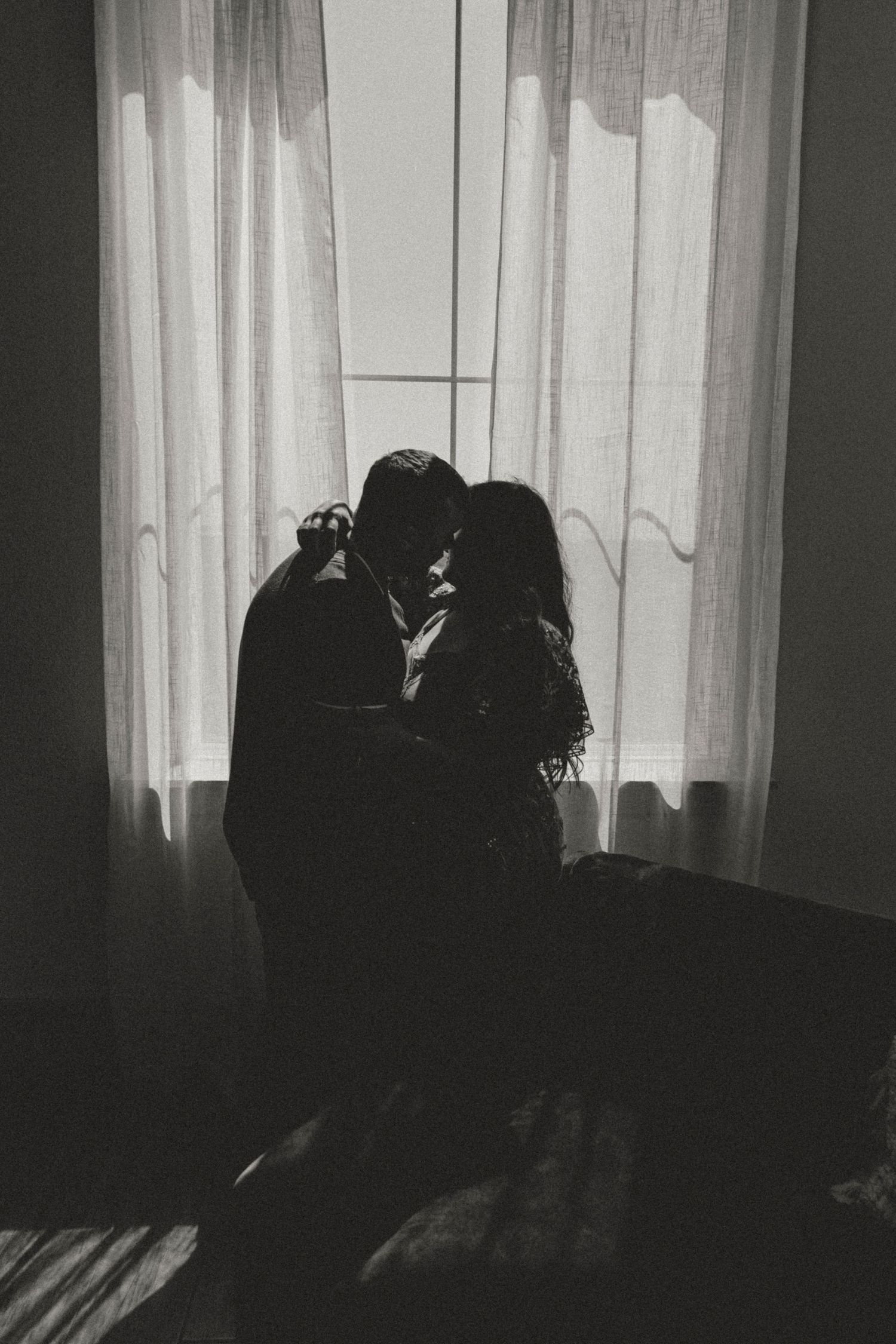 Silhouettes against backlit window creating a dramatic romantic atmosphere.