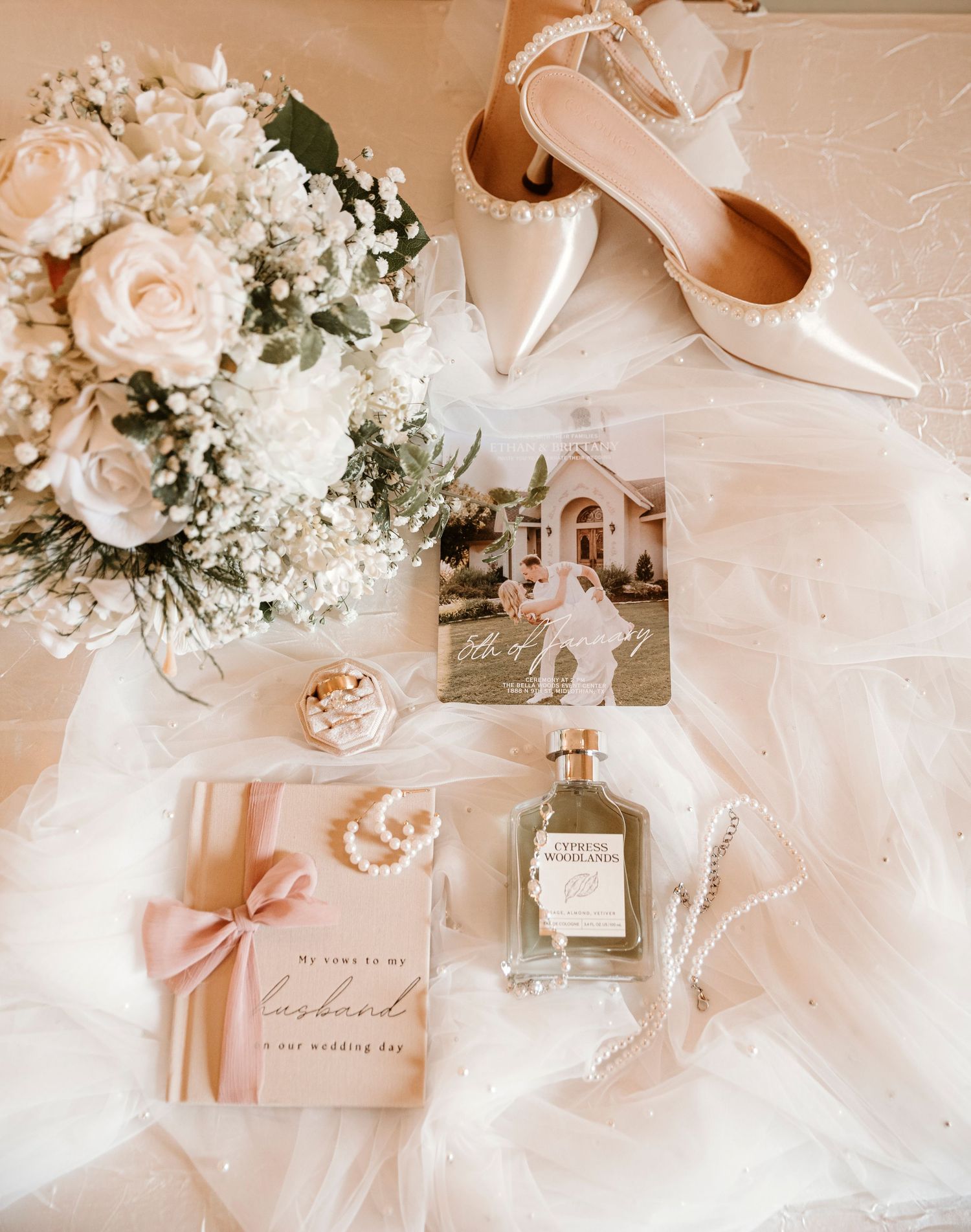 Elegant wedding details including delicate floral arrangements, perfume bottles, and blush pink accessories on white fabric.