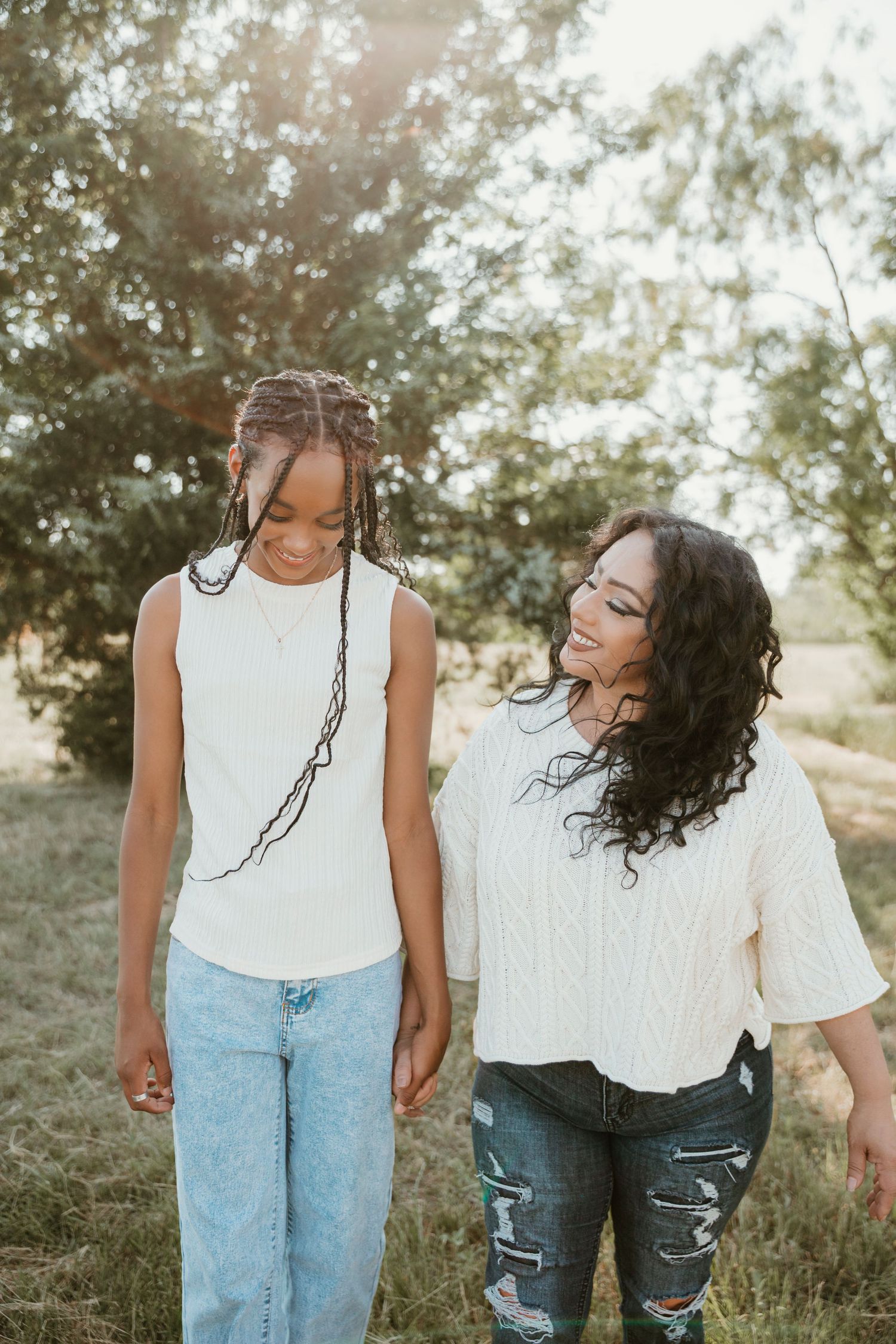 Two women walking outdoors in a sunny field, smiling and holding hands.