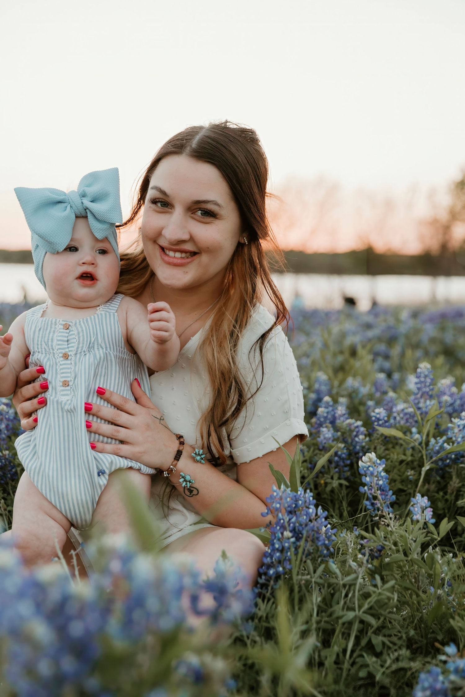 Joyful portrait in a field of bluebonnets with baby wearing blue bow headband.