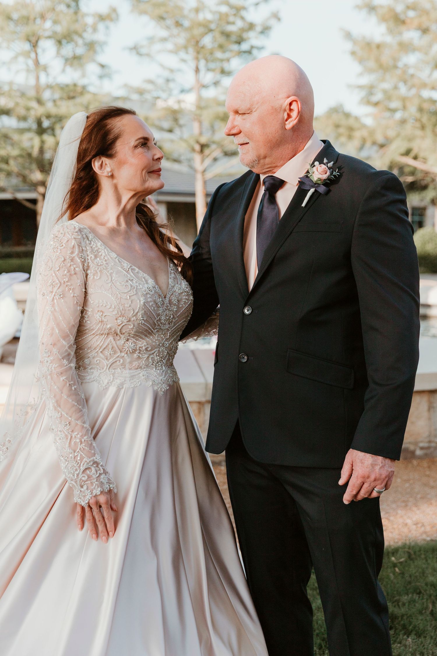 Bride in a long-sleeved lace wedding dress and groom in black suit share tender moments outdoors in autumn lighting.