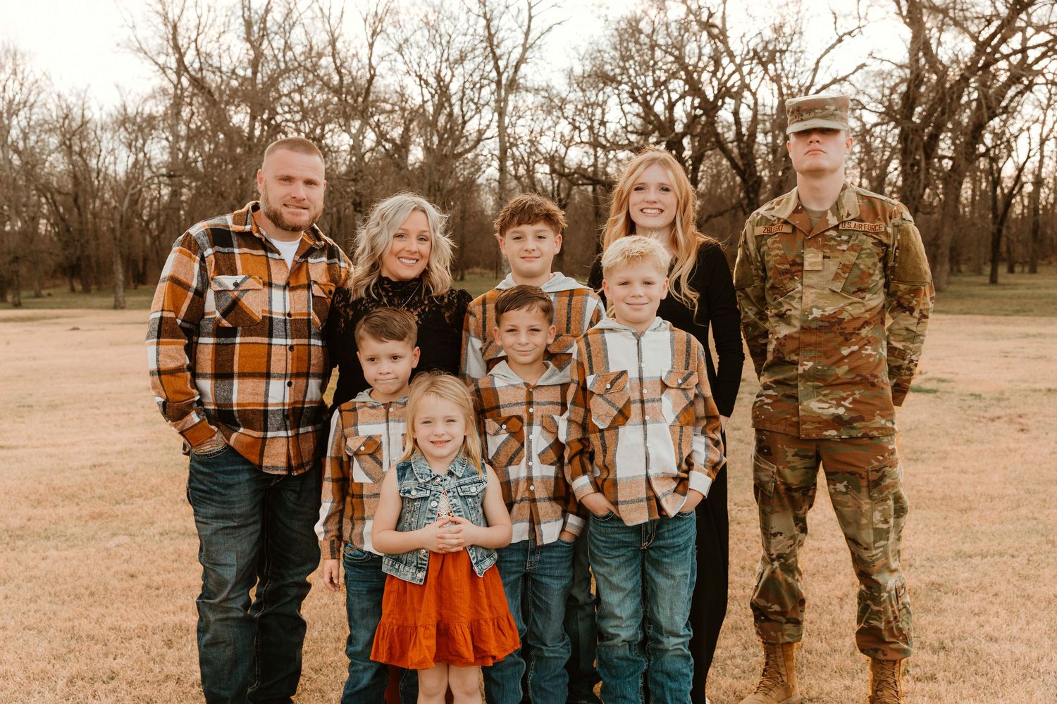 A multi-generational family group wearing plaid shirts and casual attire poses together outdoors in a rustic setting.
