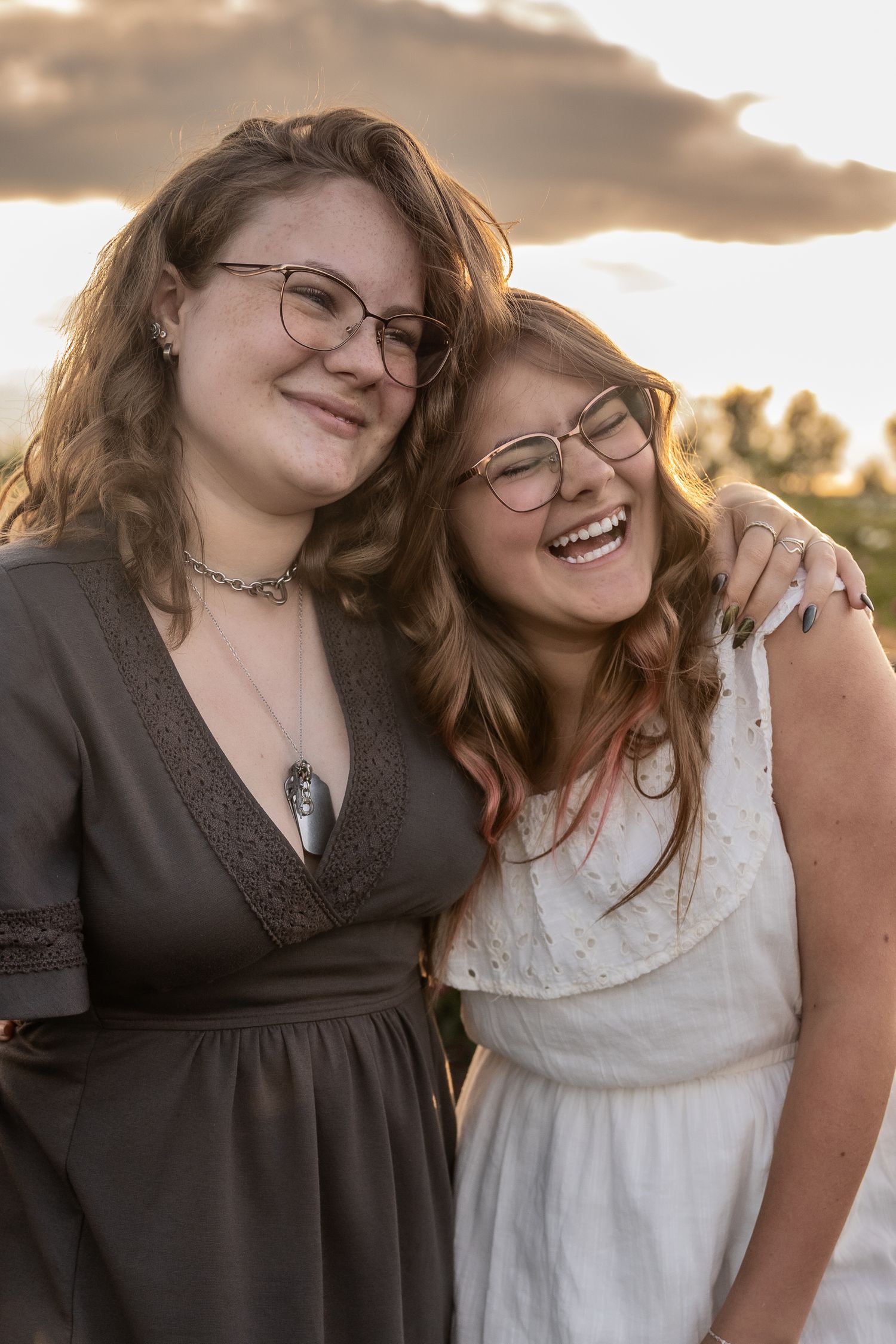 Two friends share a joyful moment together at sunset while wearing casual summer outfits.