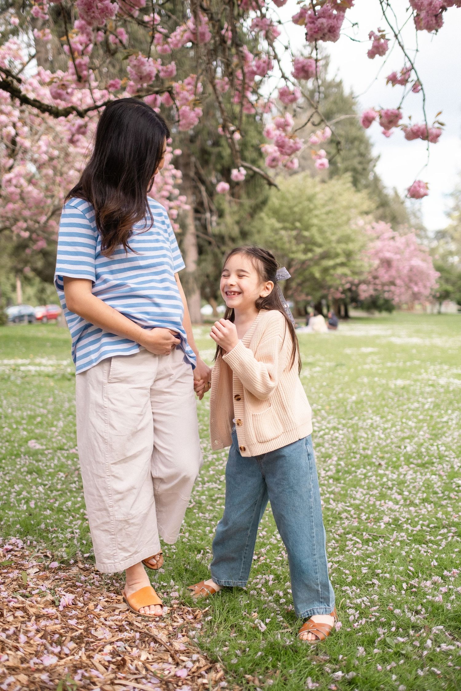 A joyful spring day with cherry blossoms overhead as two people share playful moments in a field of daisies.