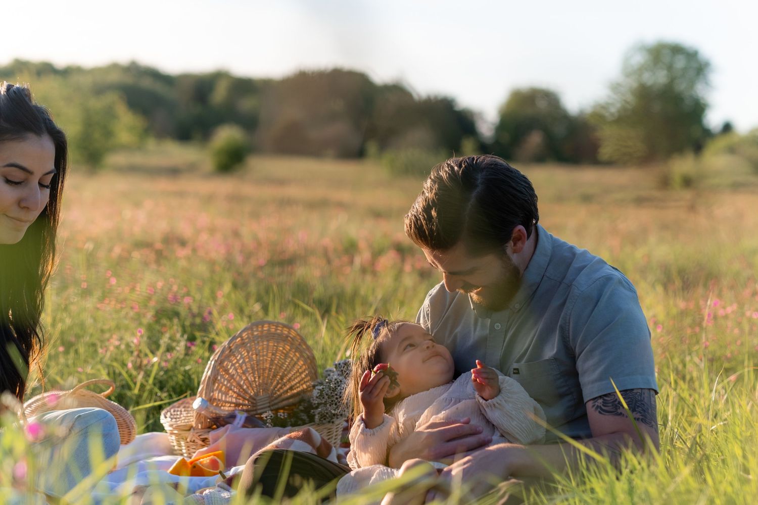 Family having a summer picnic in a field with a wicker basket during sunset.