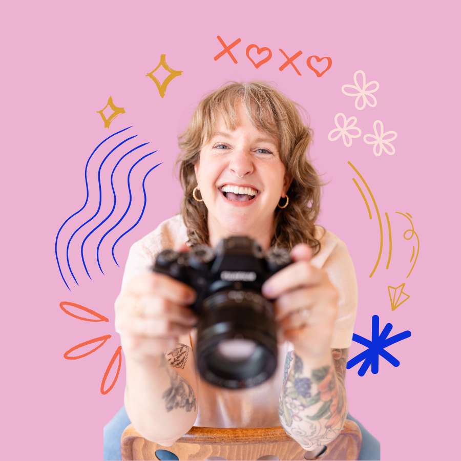 Smiling woman with tattoos holding a camera toward viewer on pink background with colorful doodles.