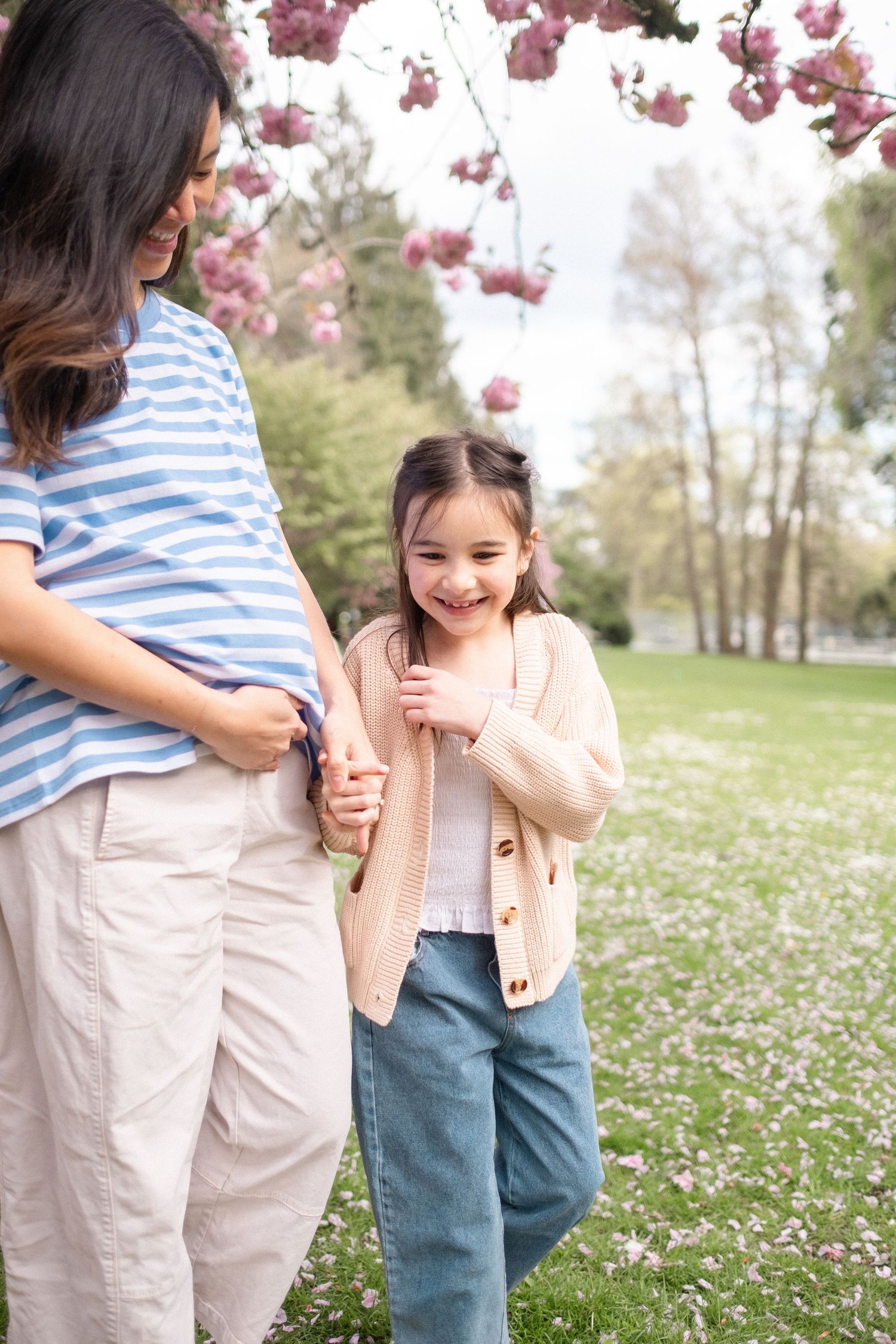A joyful moment shared between two people under pink cherry blossoms with white petals scattered on green grass.