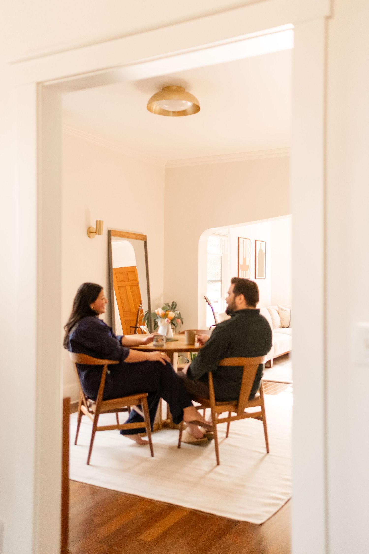Two people sit in mid-century modern chairs having a conversation in a bright, minimalist interior space.