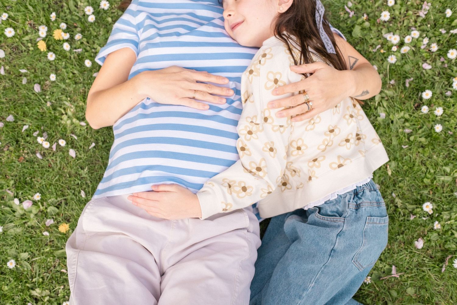 A couple lies together in a field of white daisies wearing blue and white striped shirts and jeans.