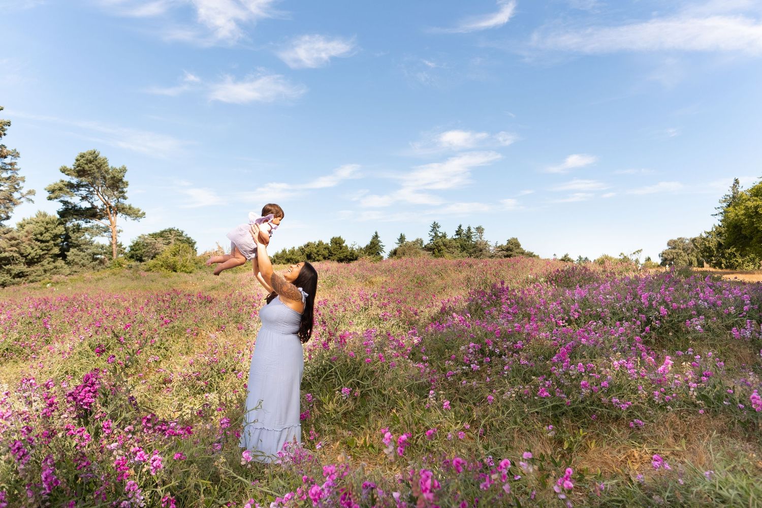 Two people embrace in a romantic pose among vibrant purple wildflowers in a scenic meadow on a sunny day.
