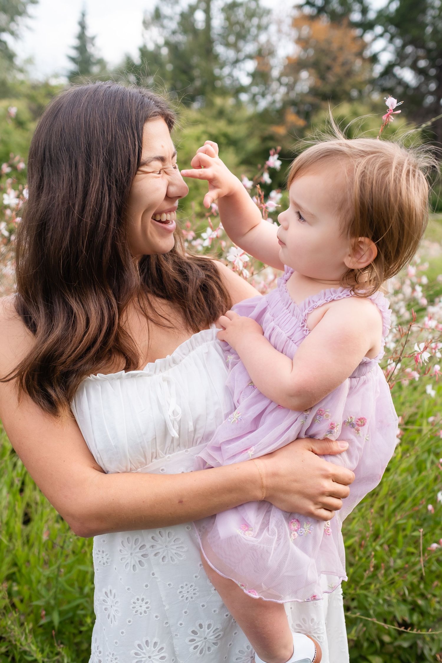 Mother and daughter share playful moments in a garden with pink flowers on a sunny summer day.