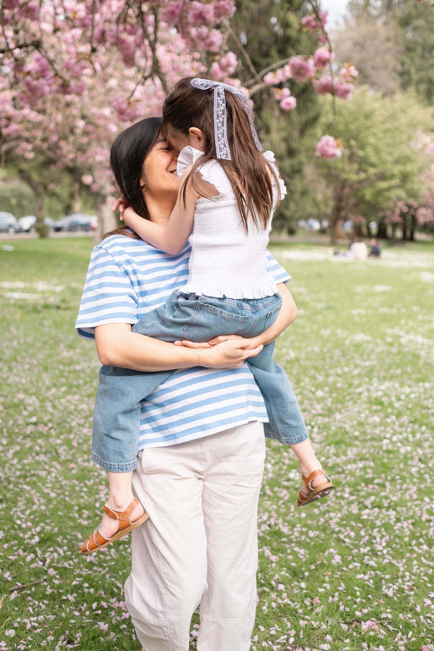 Two people embrace under blooming cherry trees in a park filled with spring flowers.