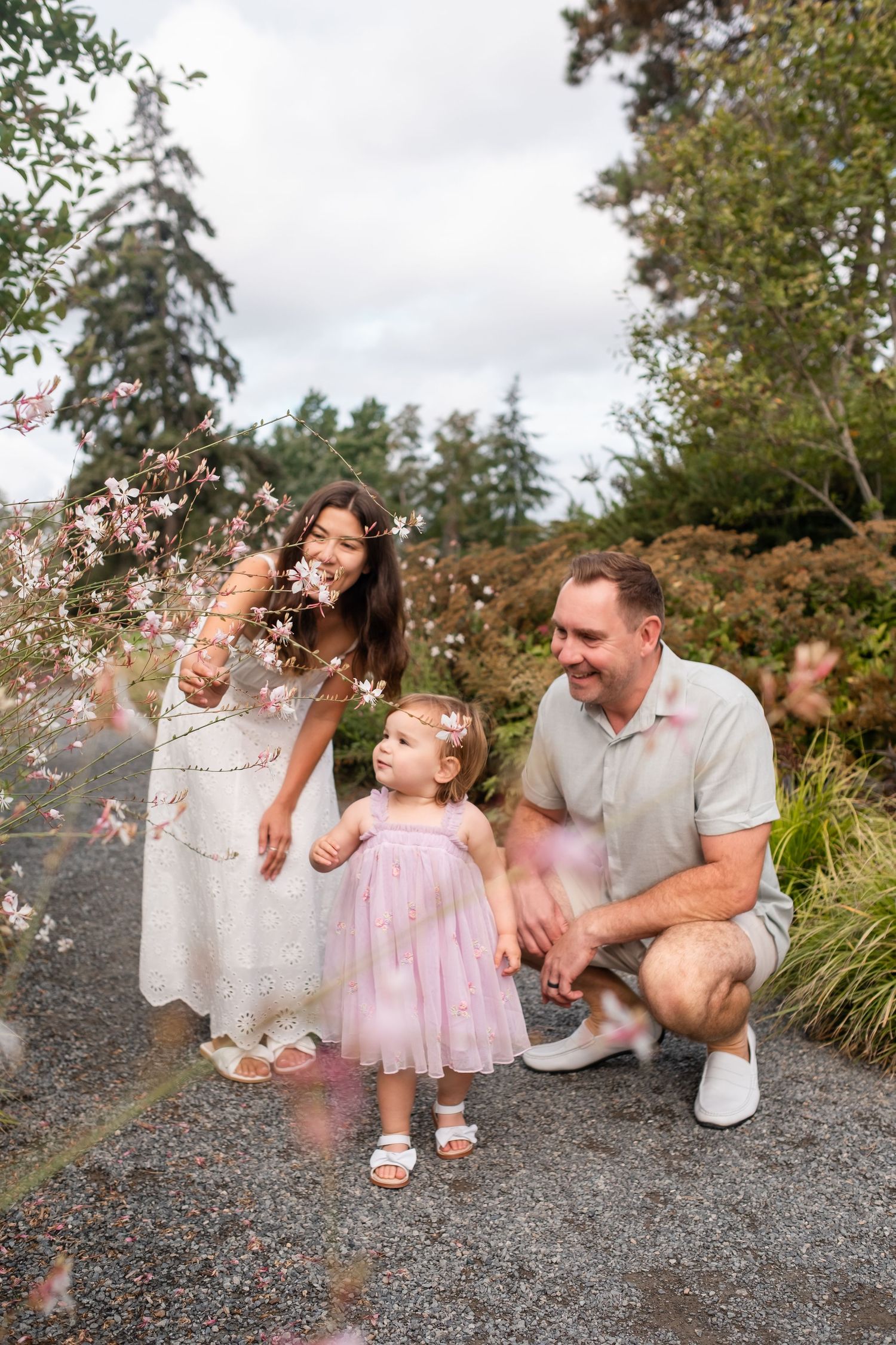 A family enjoys a playful moment together on a gravel path surrounded by greenery and floating confetti.