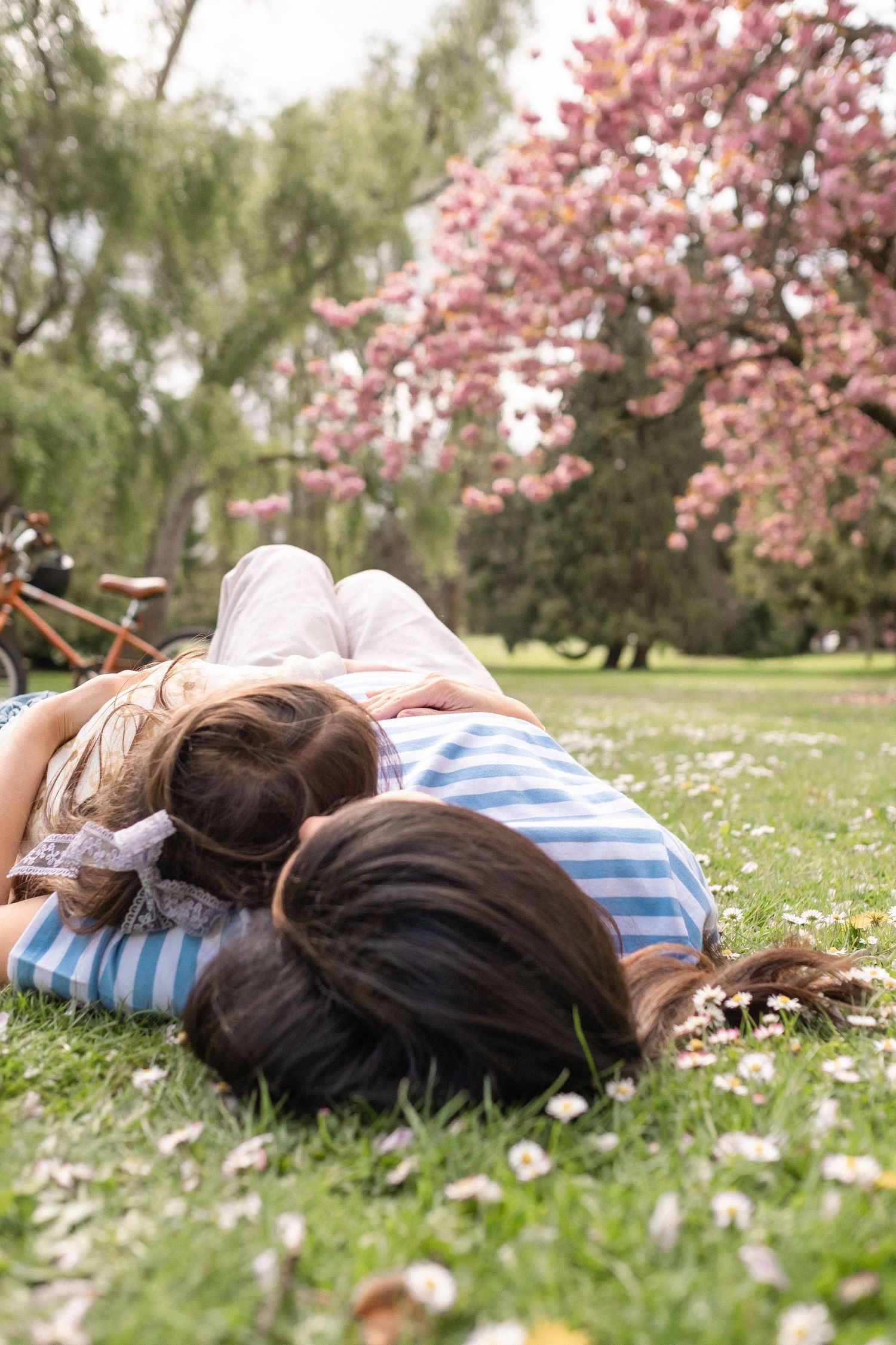 Two people lying on grass beneath pink cherry blossoms on a peaceful spring day.