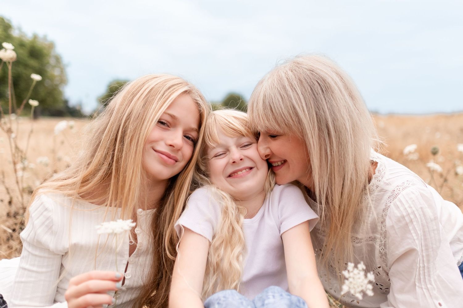 Three people with blonde hair share a joyful moment together while sitting in a sunny wheat field.