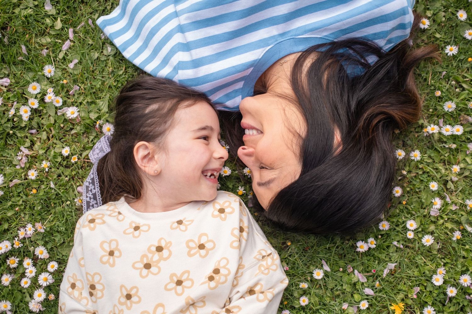 Two people lying on grass covered in small white flowers wearing casual blue and white striped clothing.