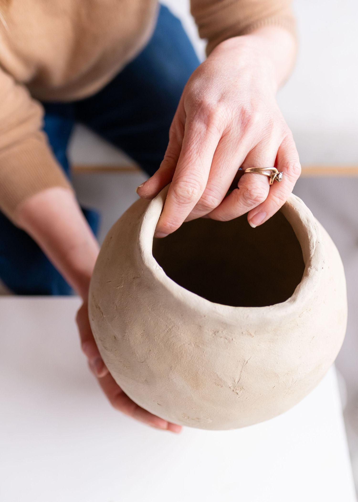 Hands hold and shape a handmade white ceramic pot showing craftsmanship details.