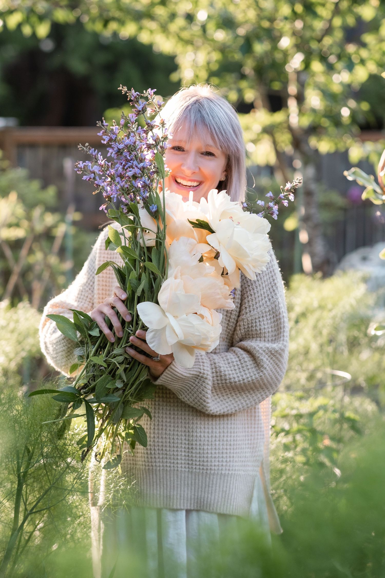 Happy woman holding a bouquet of white peonies and purple flowers in a garden.
