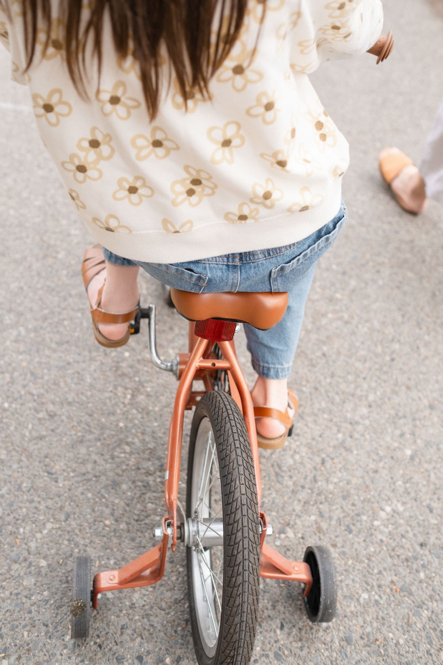 Close-up view of someone riding an orange vintage bicycle with training wheels.
