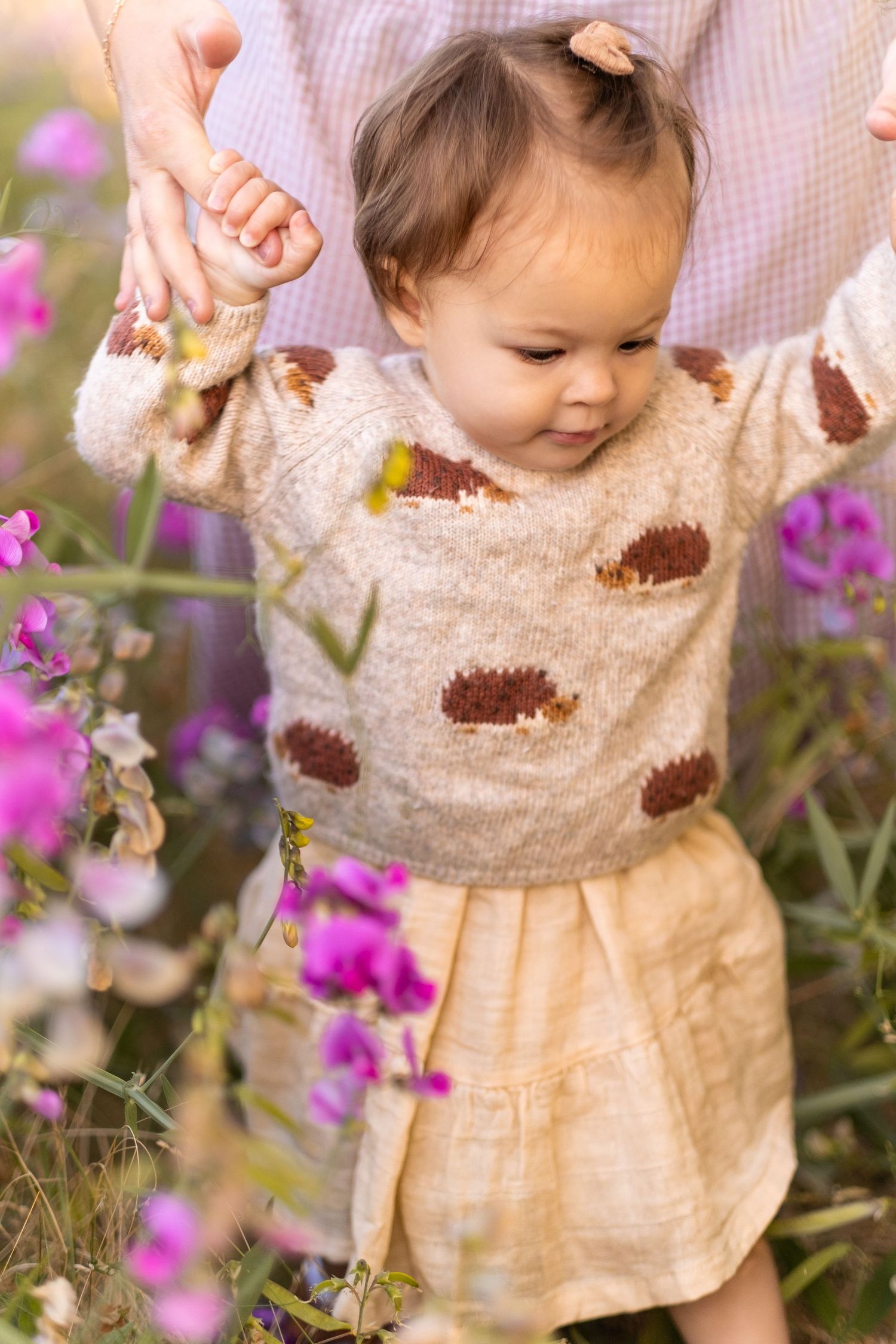A brown sweater and yellow skirt outfit shown against vibrant purple flowers in a garden setting.