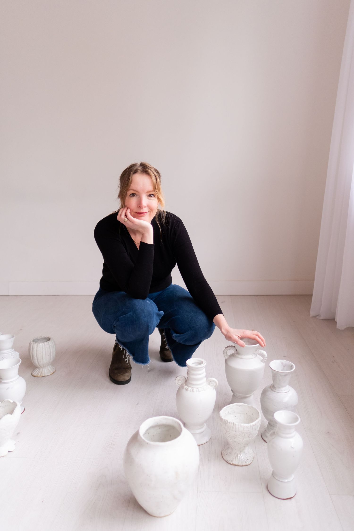 An artisan arranges white ceramic vessels on a light colored floor in a bright studio space.