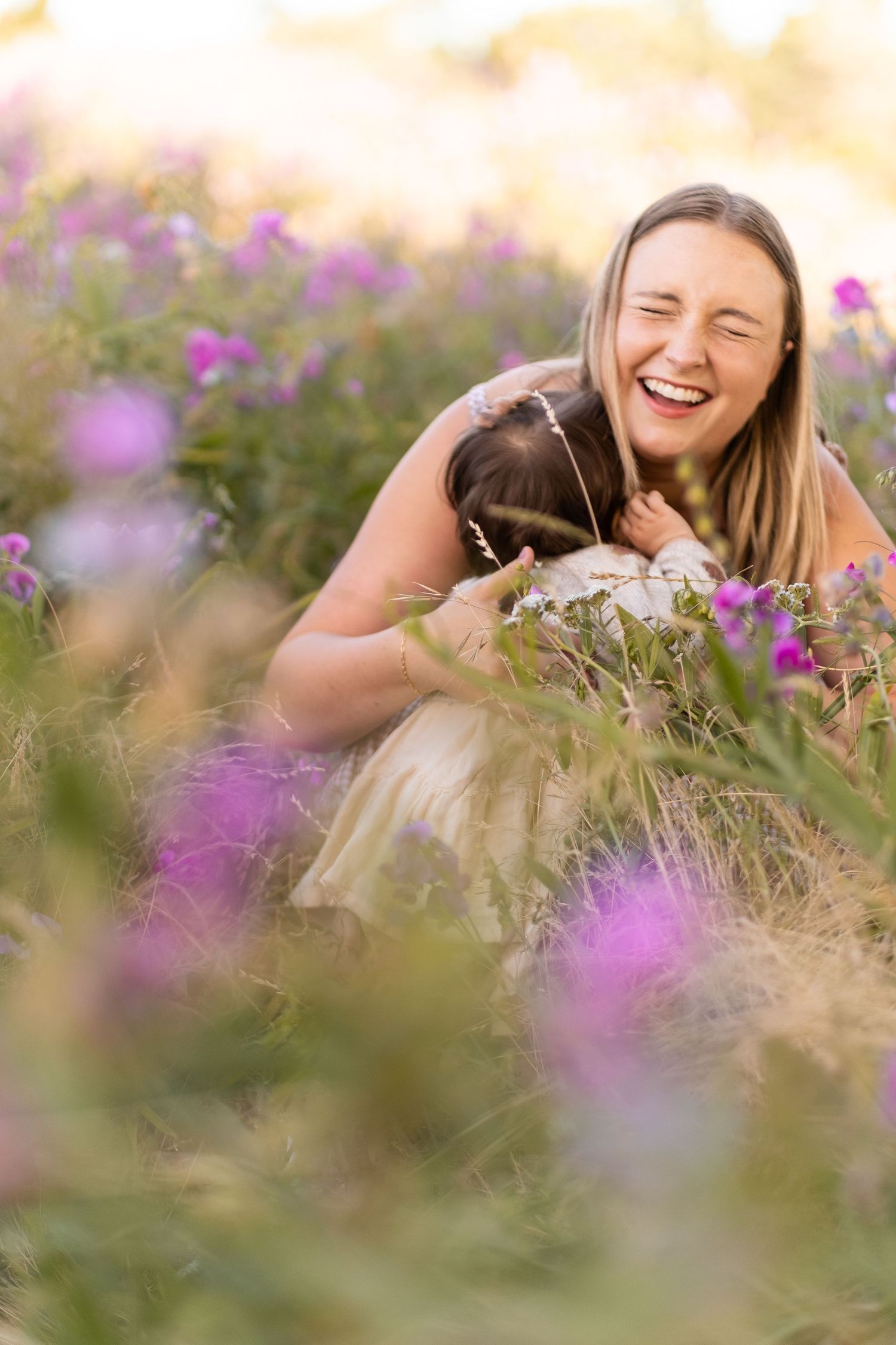 A person laying in a meadow of purple wildflowers laughs joyfully while enjoying a sunny summer day.