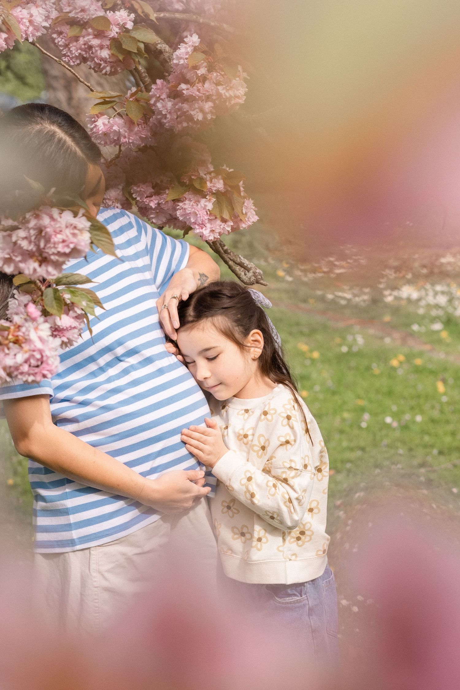 A tender moment under blooming cherry blossoms with soft pink petals and dreamy bokeh lighting.