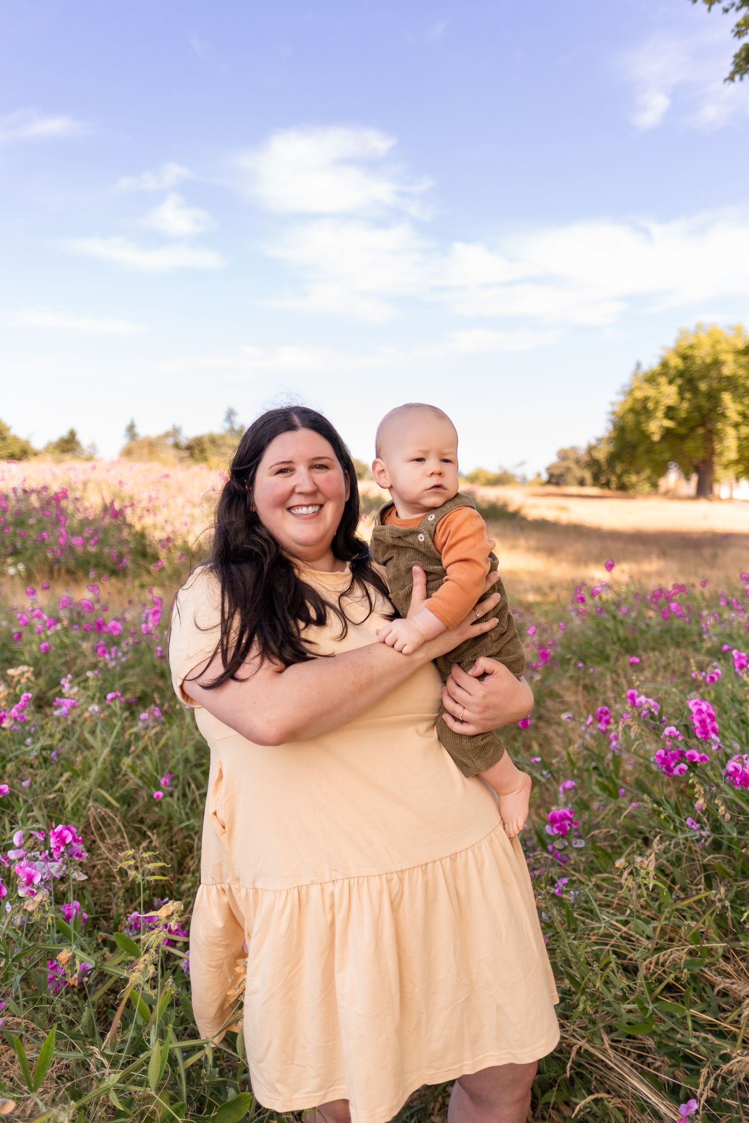 A joyful moment captured in a field of purple wildflowers on a sunny day with a cream-colored dress against blue skies.