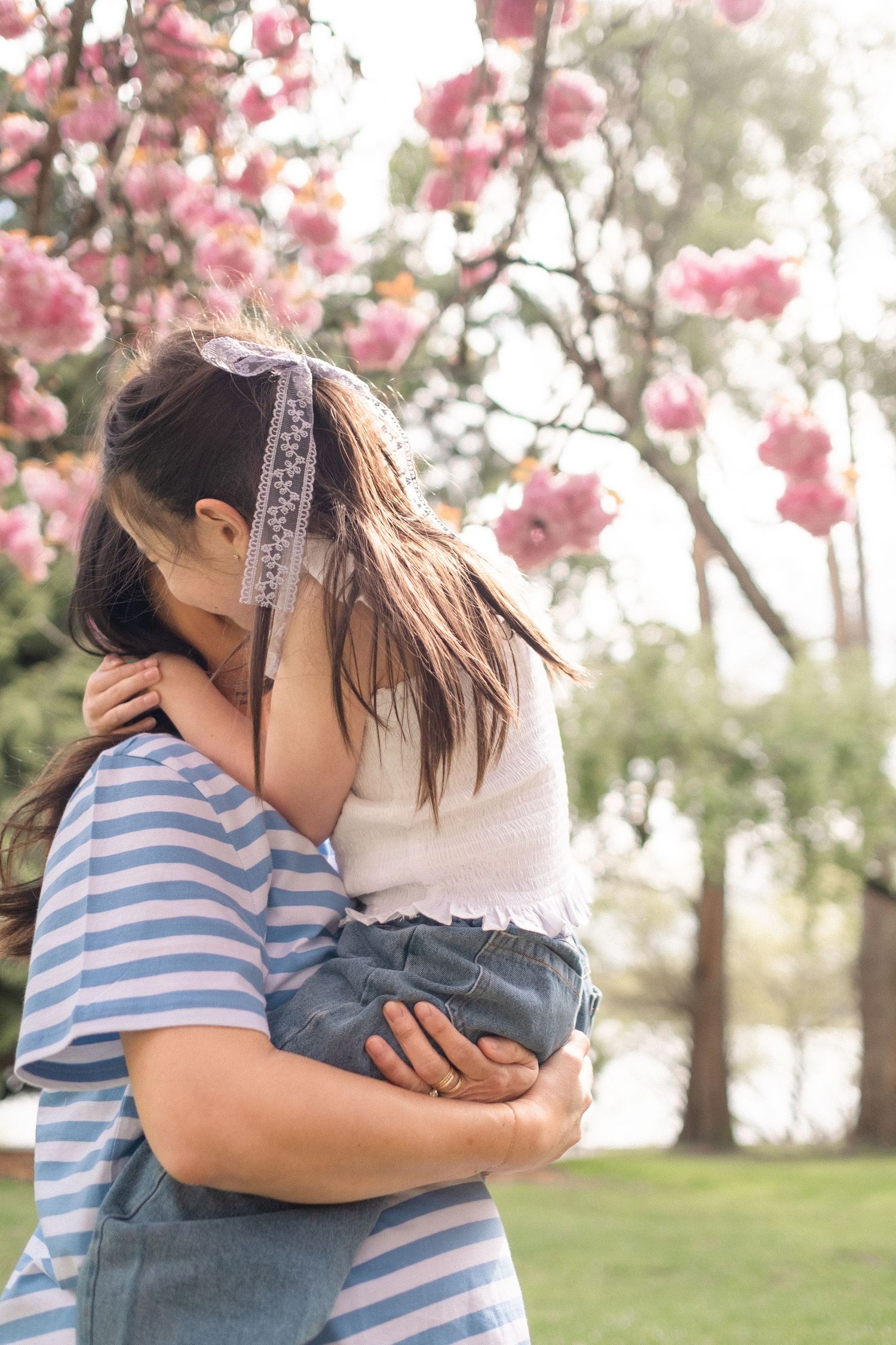 Mother and child share tender embraces under blooming pink cherry blossoms in a spring garden.