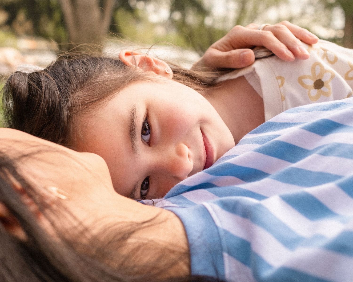 Close up of people resting on grass with blue and white striped clothing and scattered daisies.