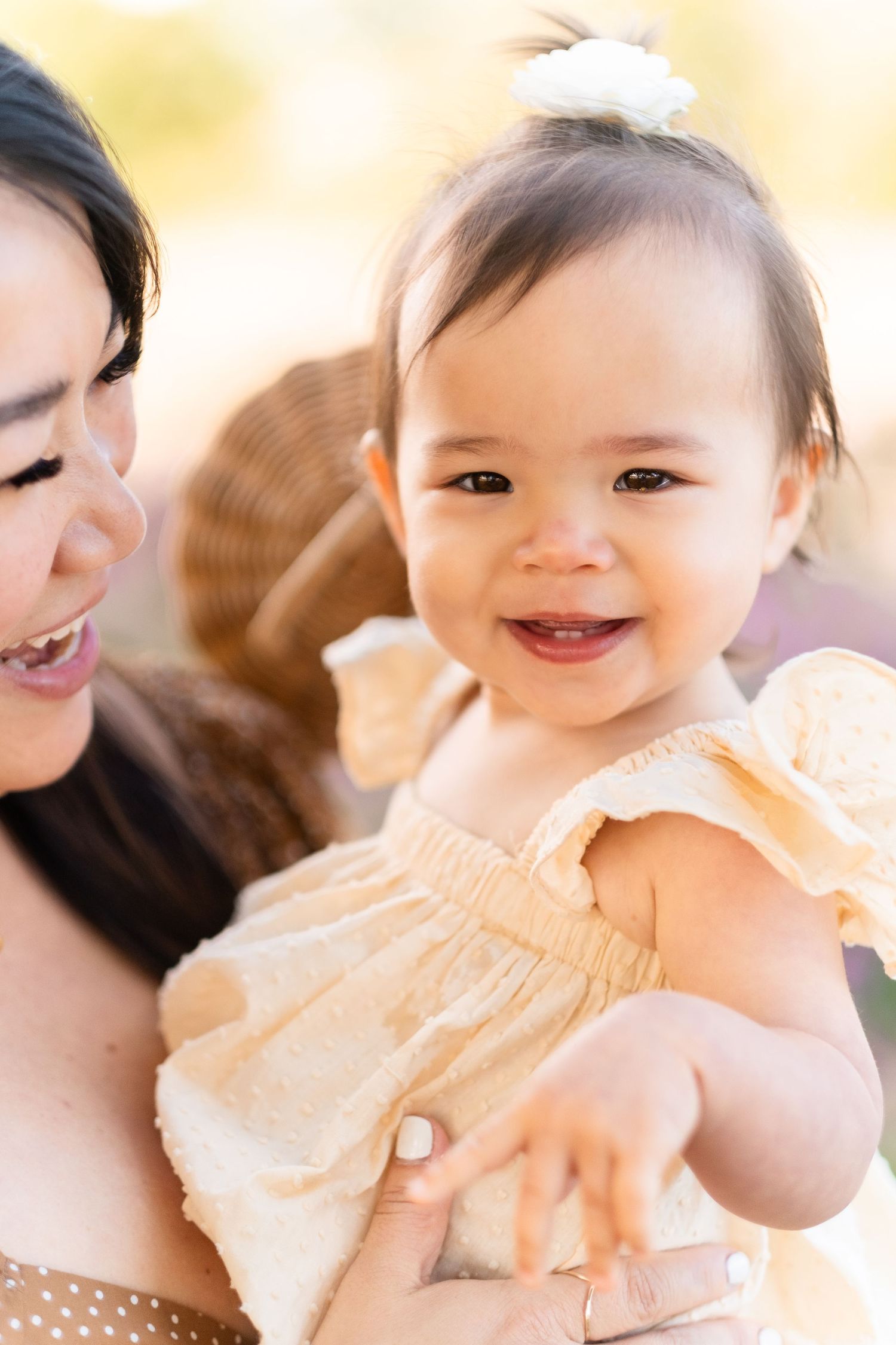 Adorable baby in a peach-colored dress smiling while being held in soft natural lighting.