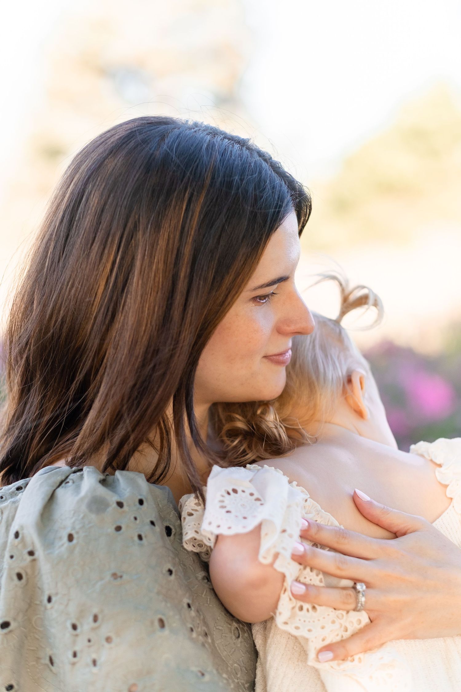 A tender moment captured in a field of purple flowers as someone holds a small child wearing delicate lace.